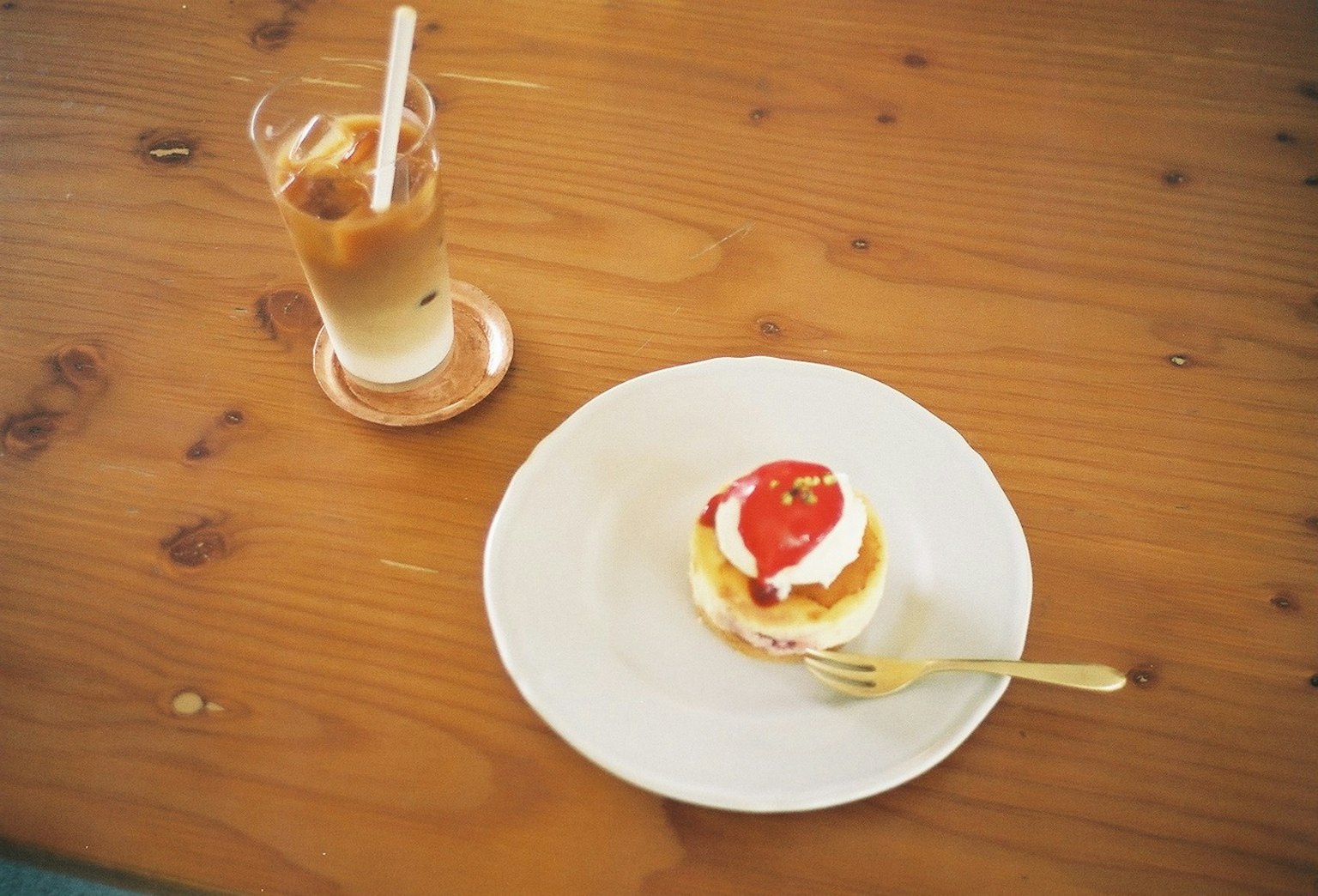Cream and strawberry sauce cake on a wooden table with iced coffee