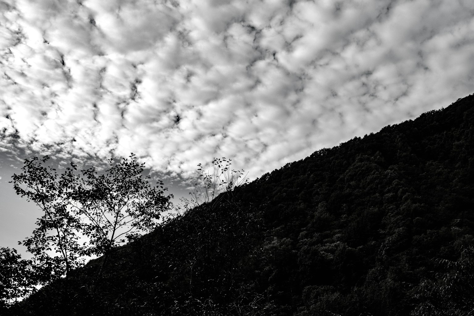 Black and white landscape featuring a silhouetted hill and a sky filled with clouds