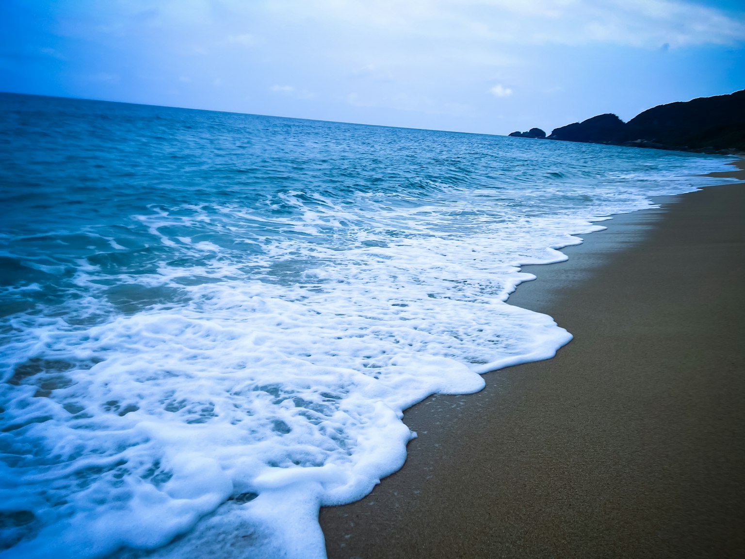 Una escena de playa tranquila con olas azules del océano golpeando suavemente la arena