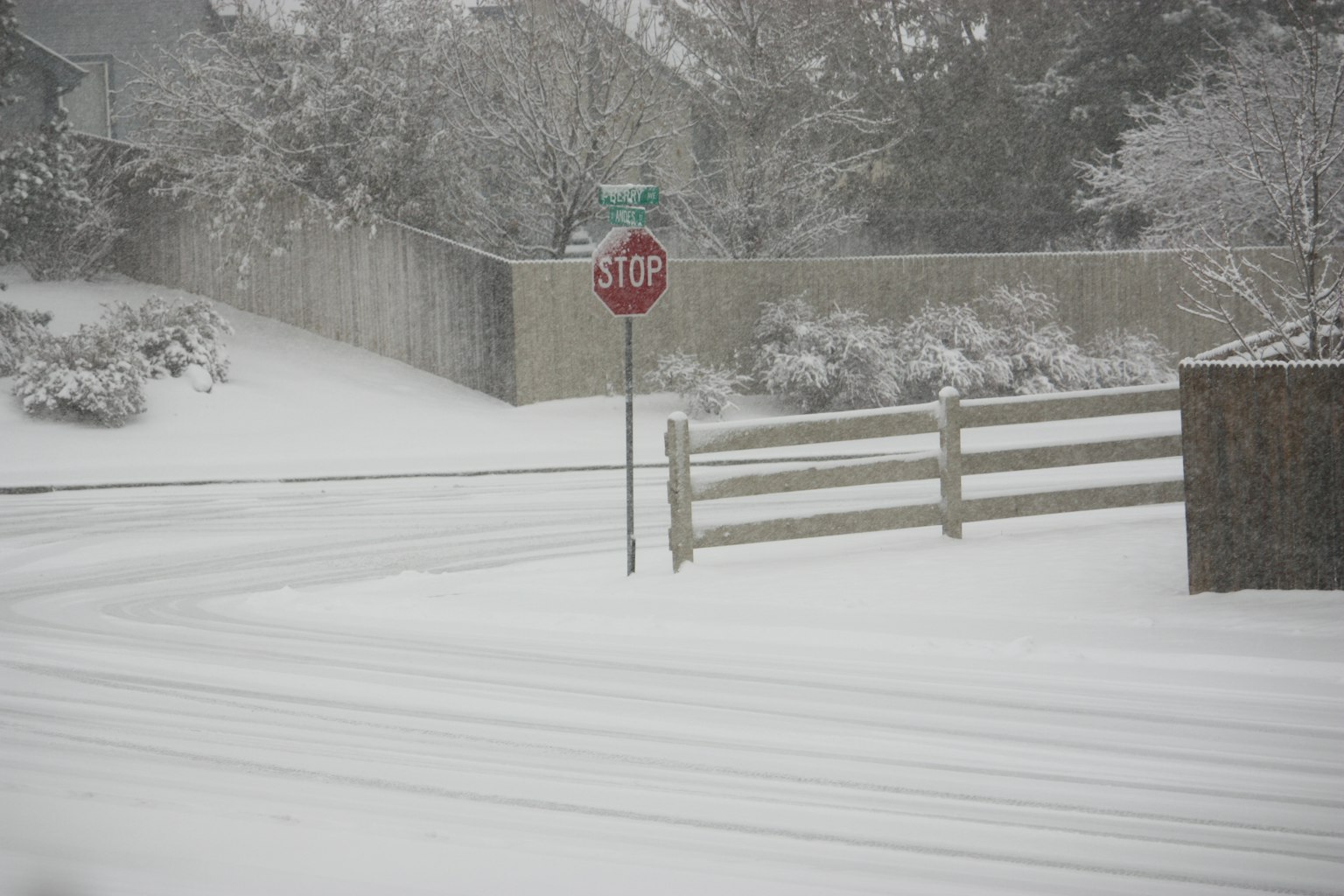 Schneebedeckte Straße mit einem Stoppschild und einem Holzzaun