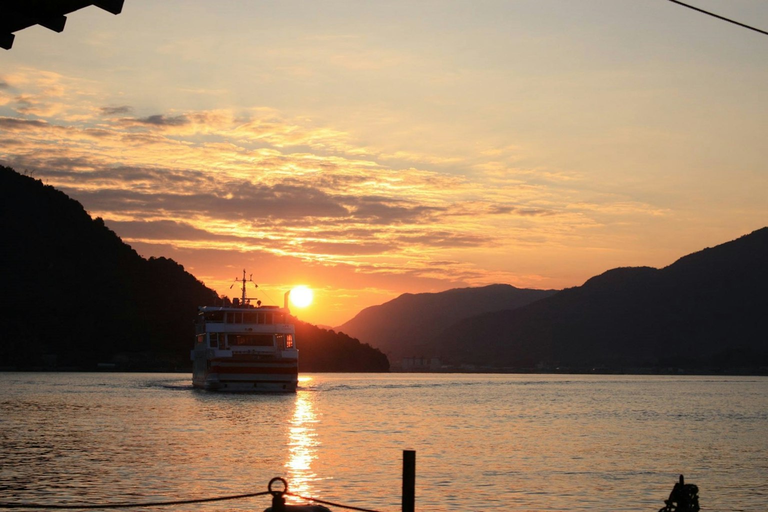 Ein Boot fährt auf einem Fluss bei Sonnenuntergang mit Bergen im Hintergrund