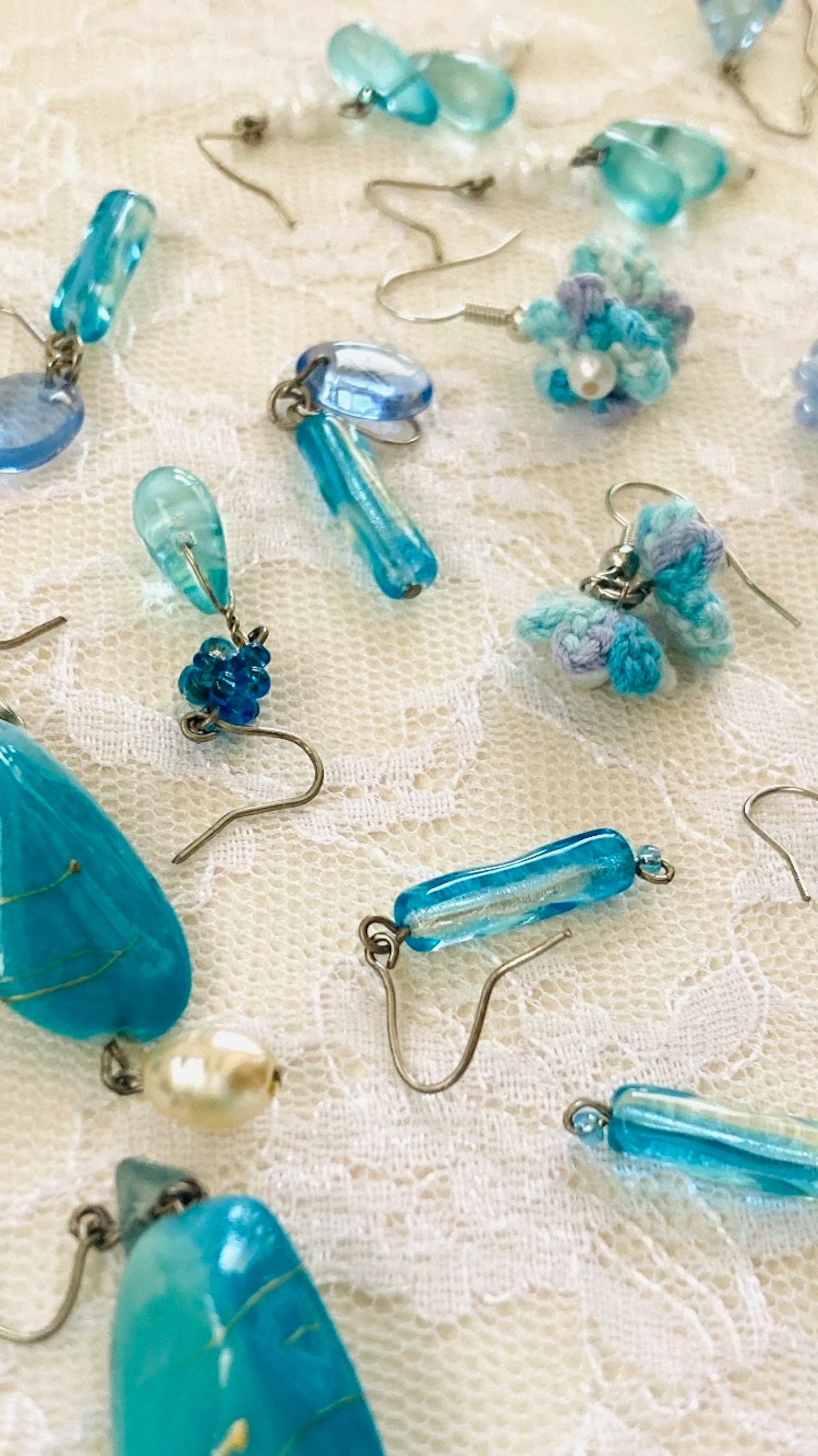 Blaue Perlenohrringe, die auf einem Spitzenstoff verstreut sind