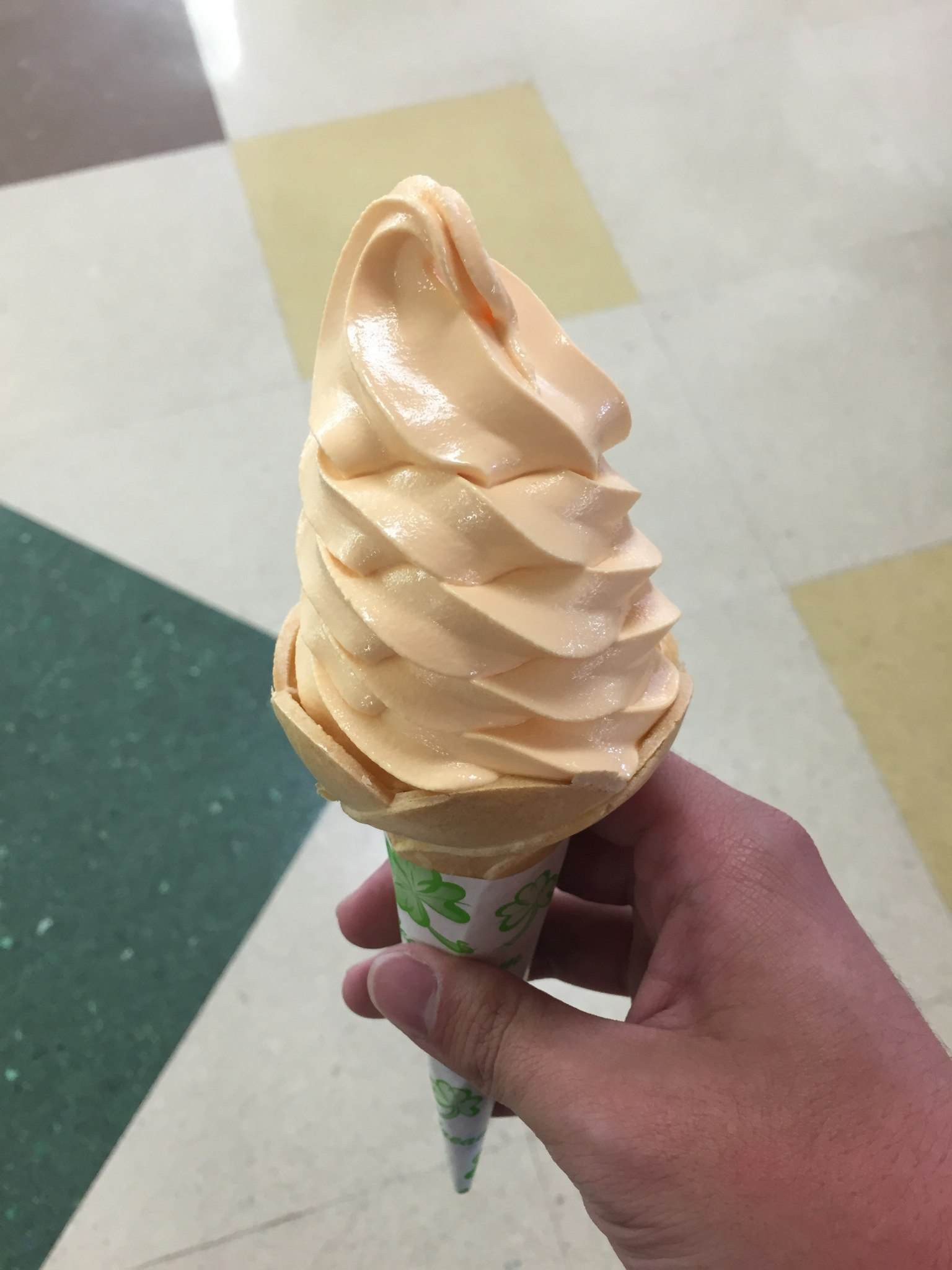 Sebuah tangan memegang es krim lembut oranye dalam kerucut