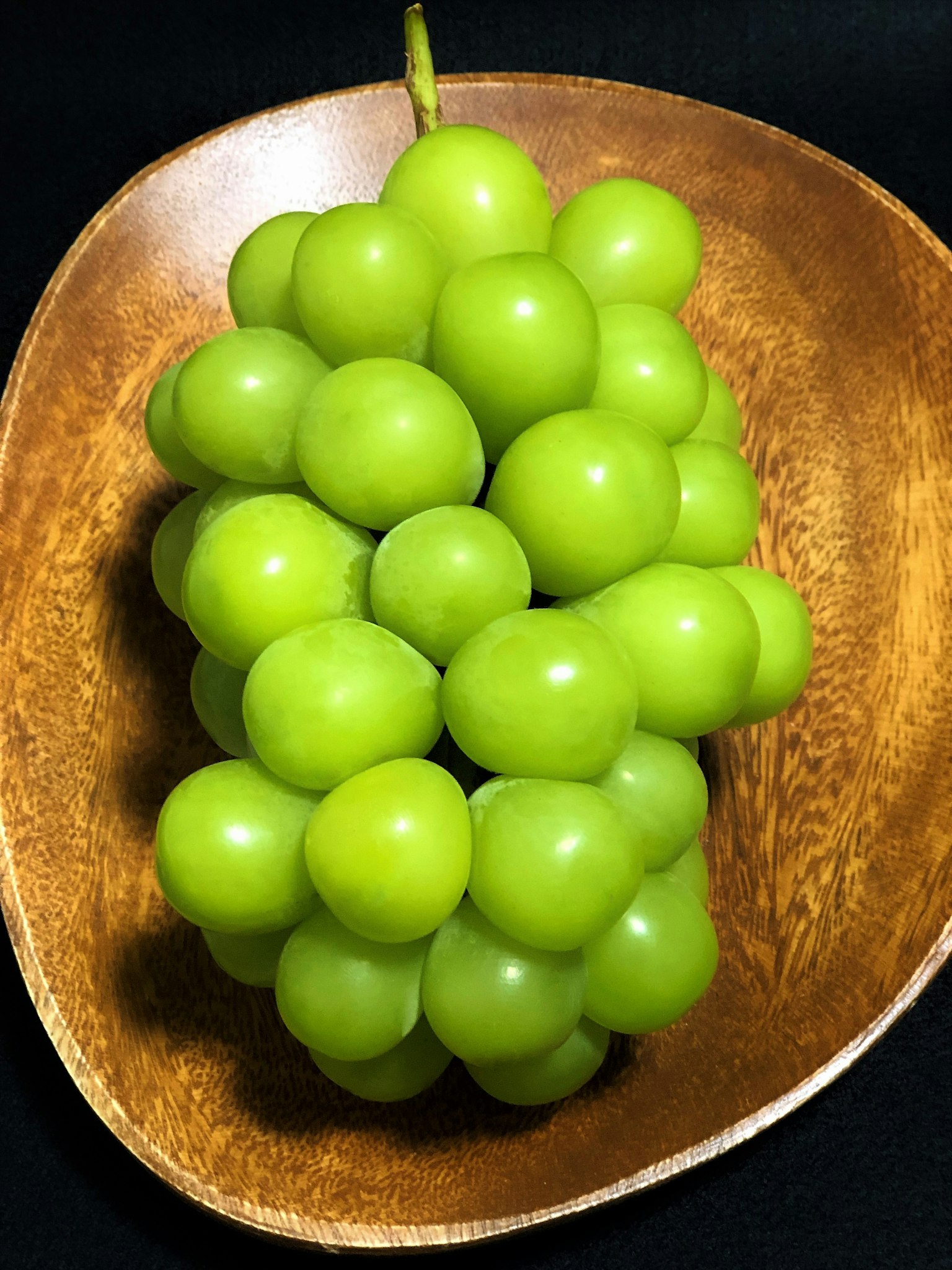A cluster of green grapes in a wooden bowl