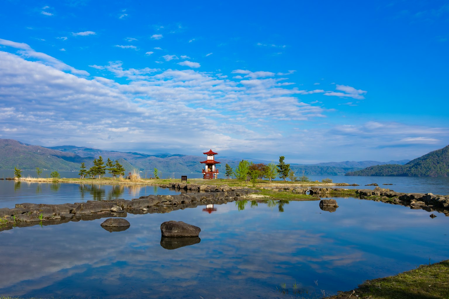 Vista panoramica del lago con un faro rosso e bianco sotto un cielo blu