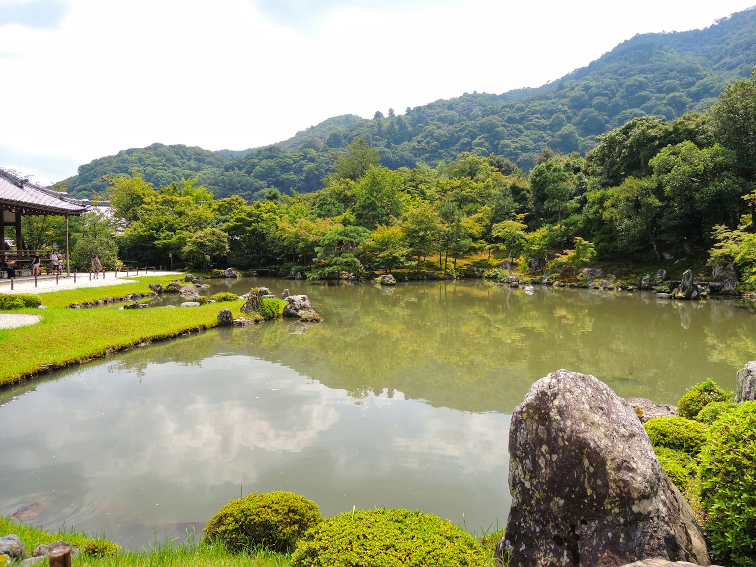 ทิวทัศน์สวนสงบพร้อมบ่อน้ำต้นไม้เขียวขจีและภูเขาในพื้นหลัง