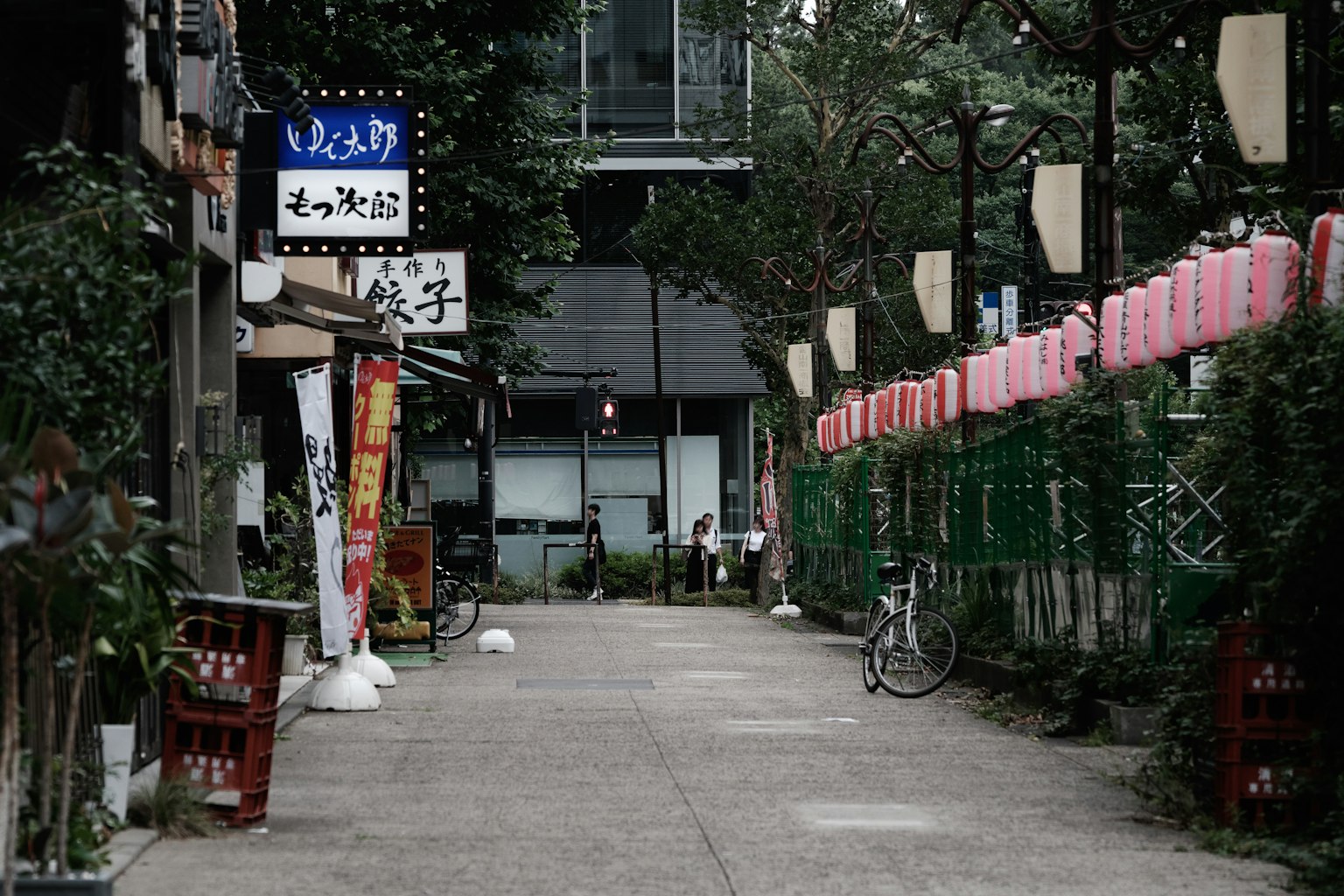 Jalan sempit di Tokyo dengan papan nama restoran dan tanaman hijau