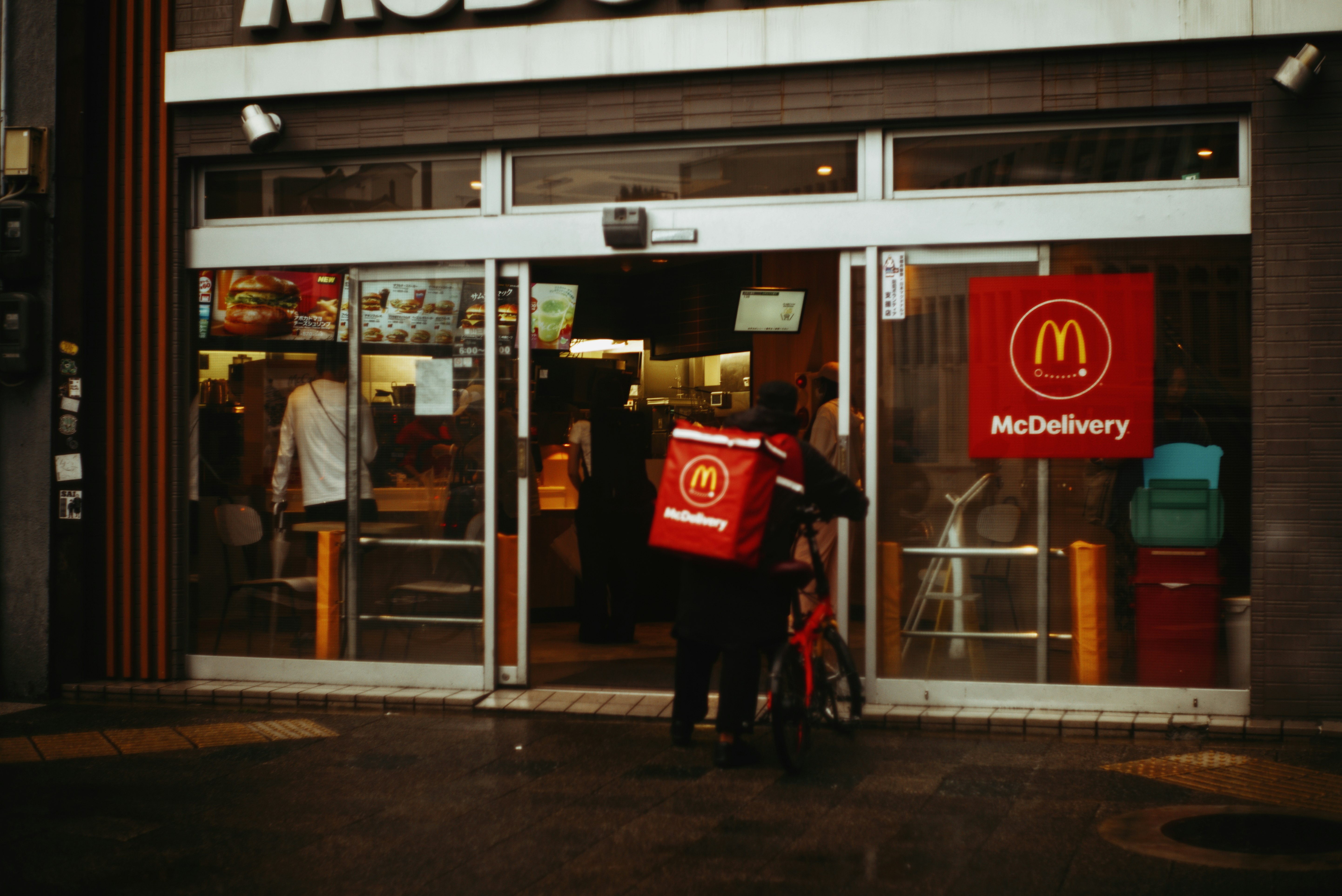 雨の夜のマクドナルド店先と配達バッグの人
