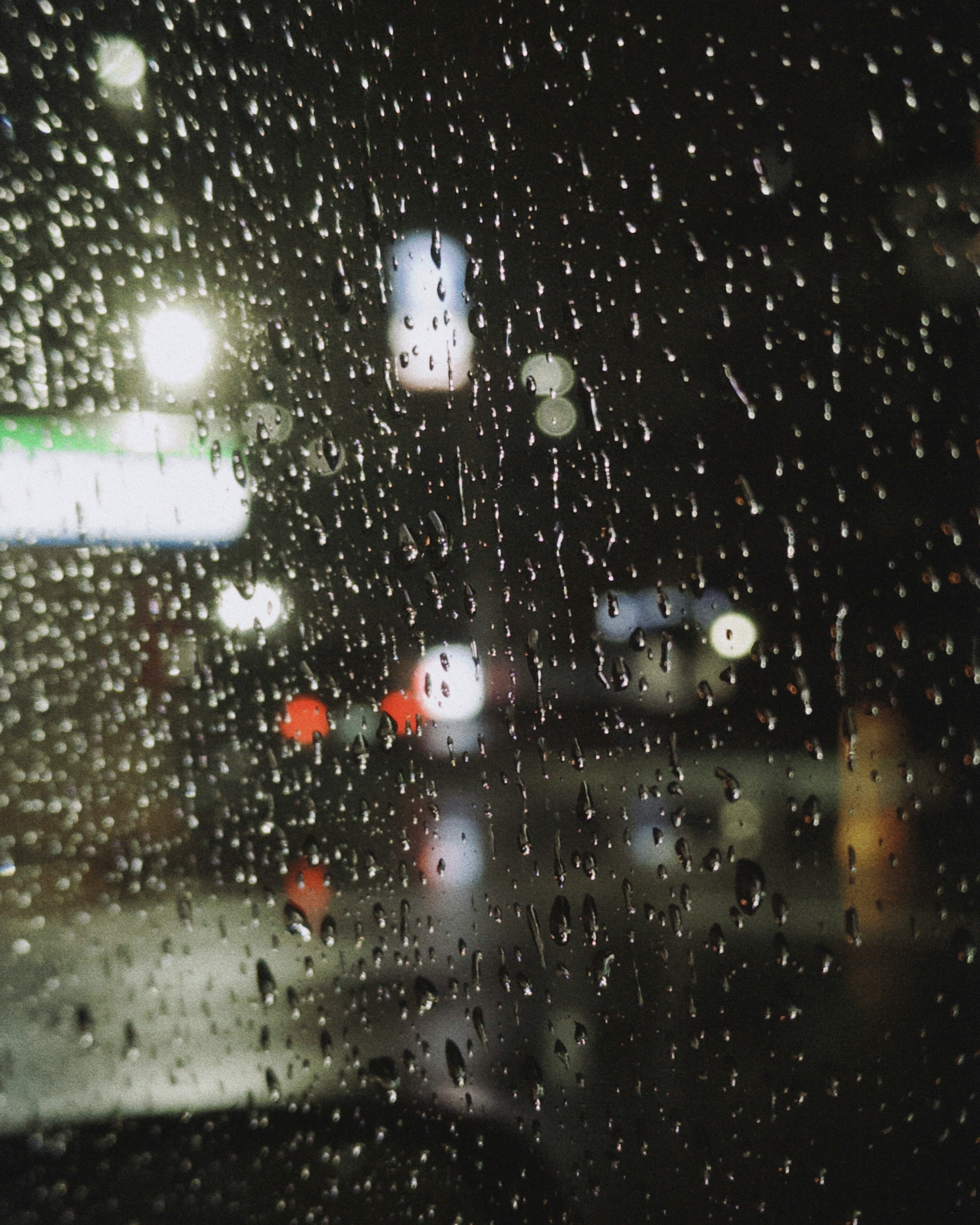 雨粒の窓ガラス越しに街灯がにじむ夜の風景
