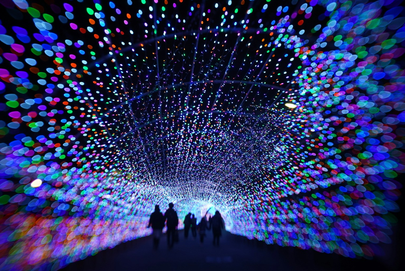 Silhouette di persone che camminano attraverso un tunnel di luci colorate