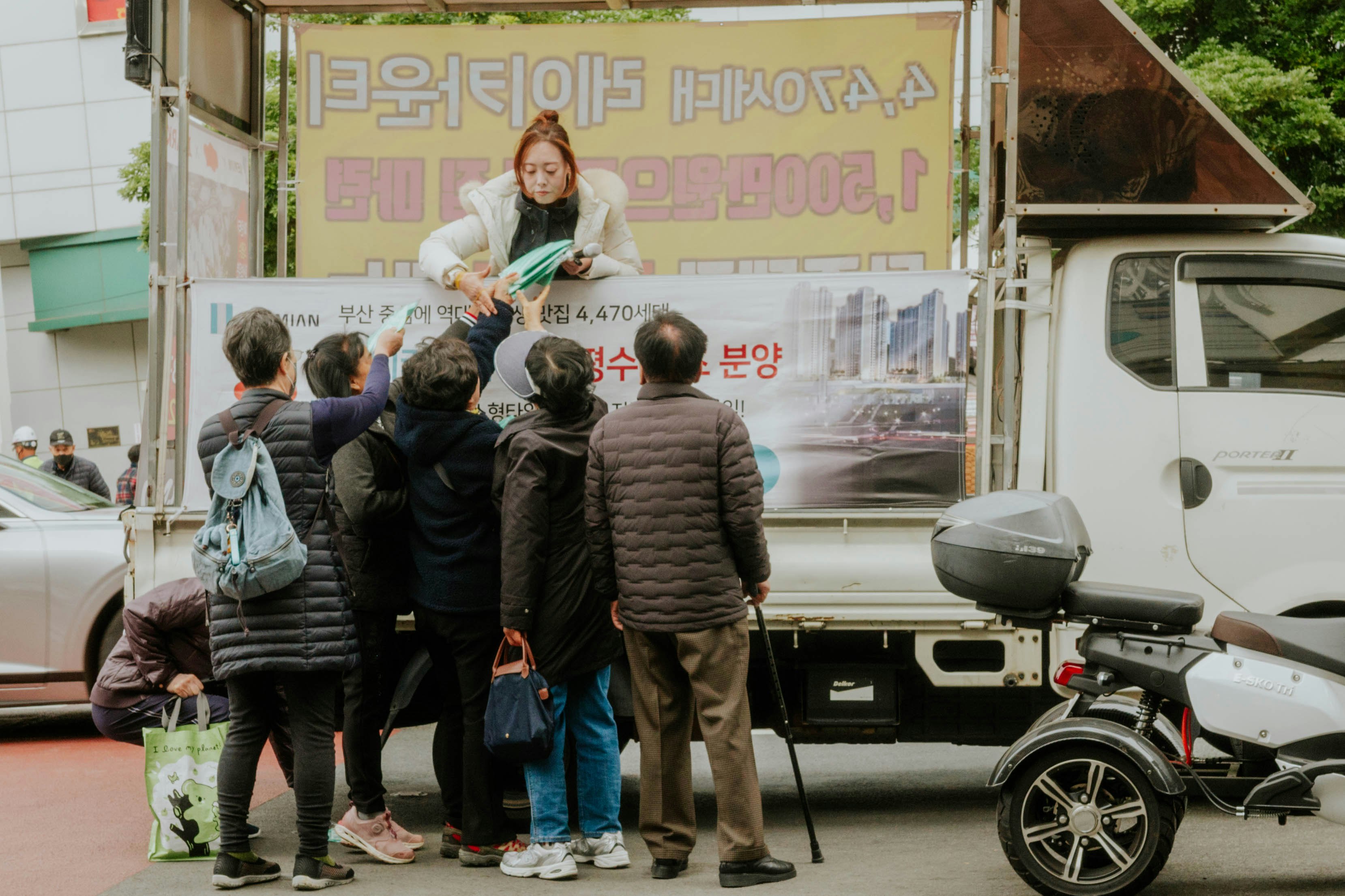 路上で配布を受け取る人々とバイクのあるトラック前の光景