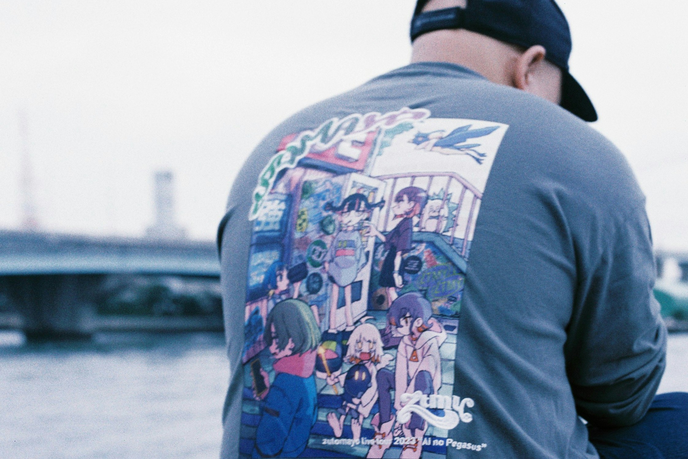 背中にアニメ風プリントのTシャツを着た人物の後ろ姿
