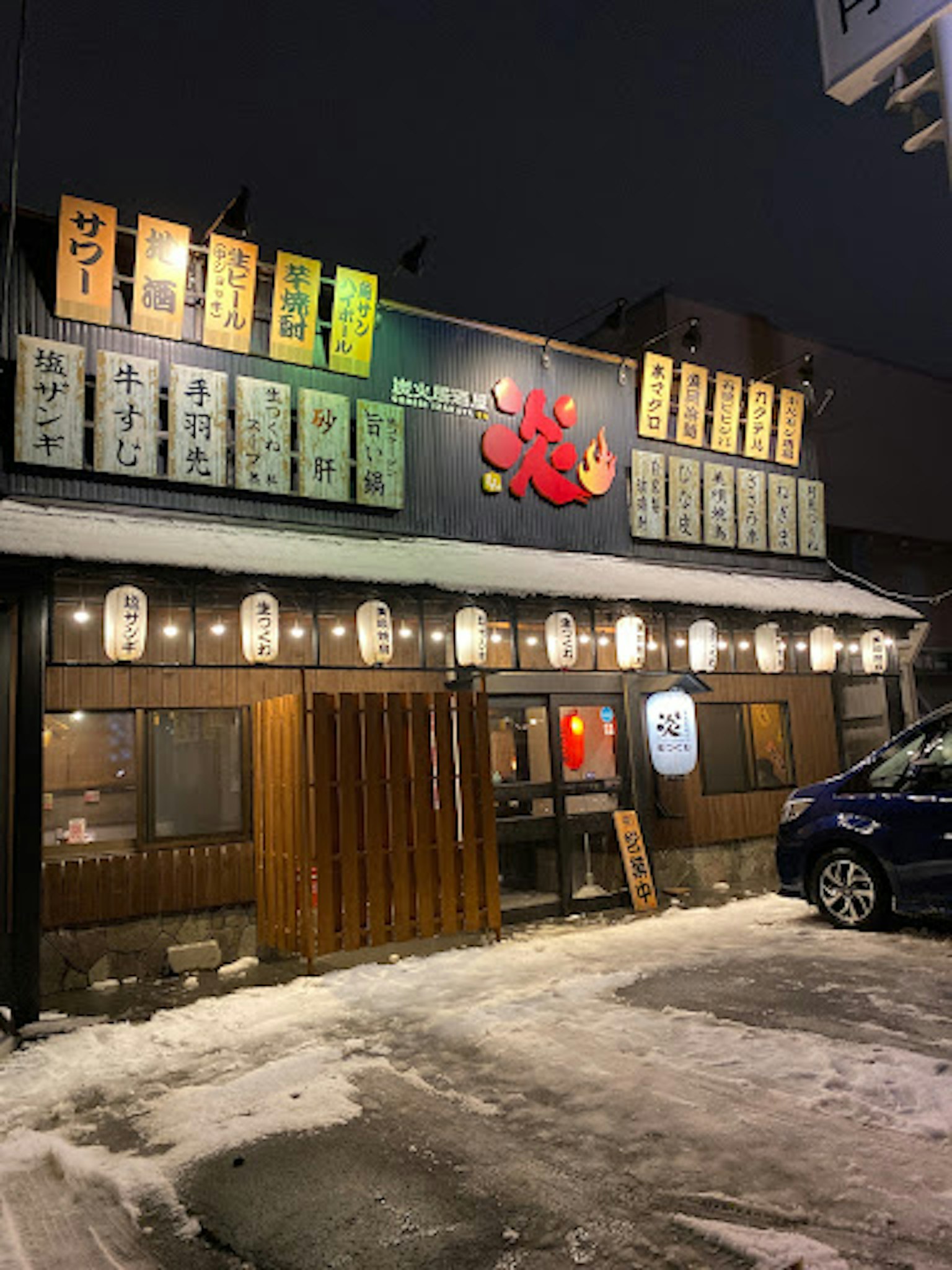 Extérieur d'un izakaya japonais dans la neige avec des enseignes lumineuses et un éclairage chaleureux
