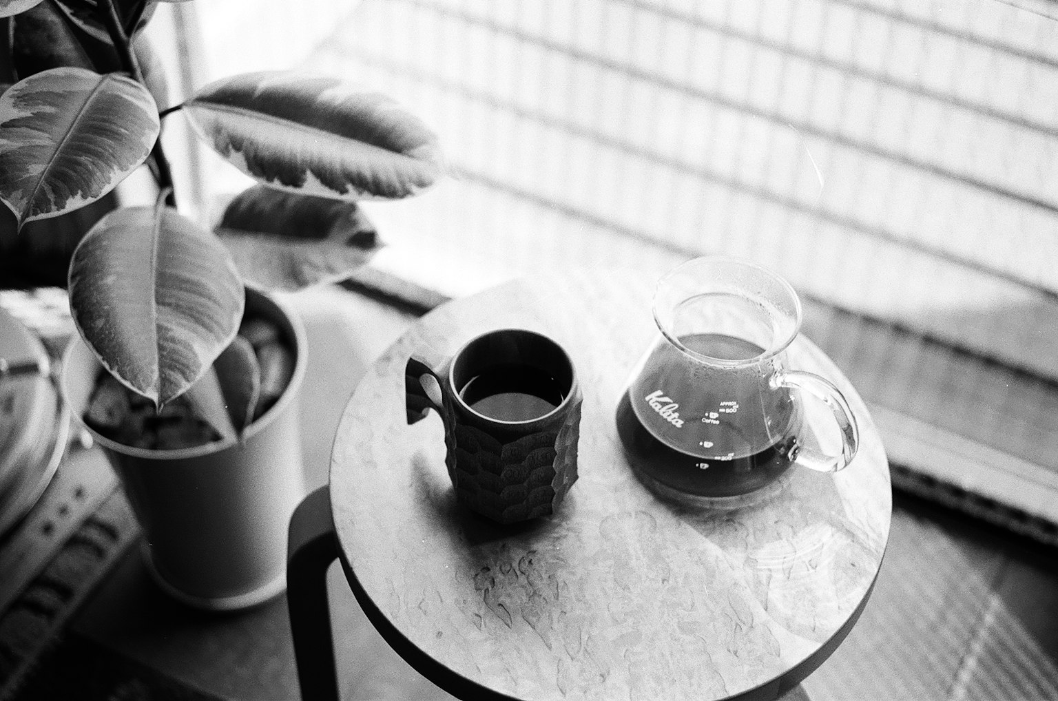 Tazza e caffettiera su un tavolo con una foglia di pianta sullo sfondo foto in bianco e nero