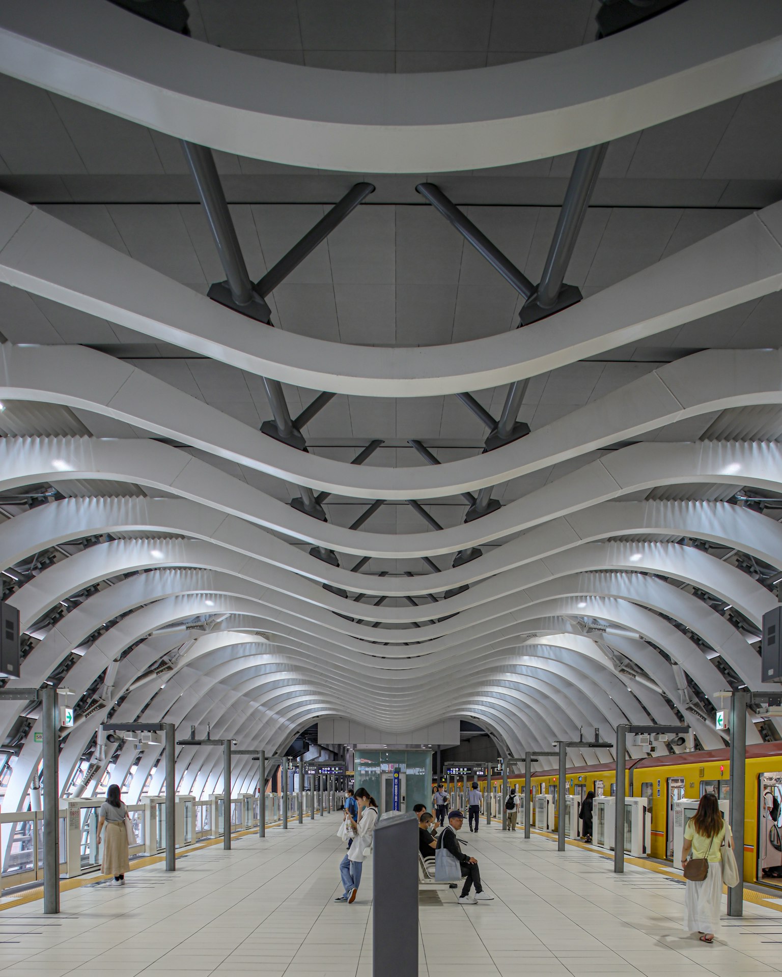 現代的な駅の内部構造、波状の天井、白い色調、乗客が待機中