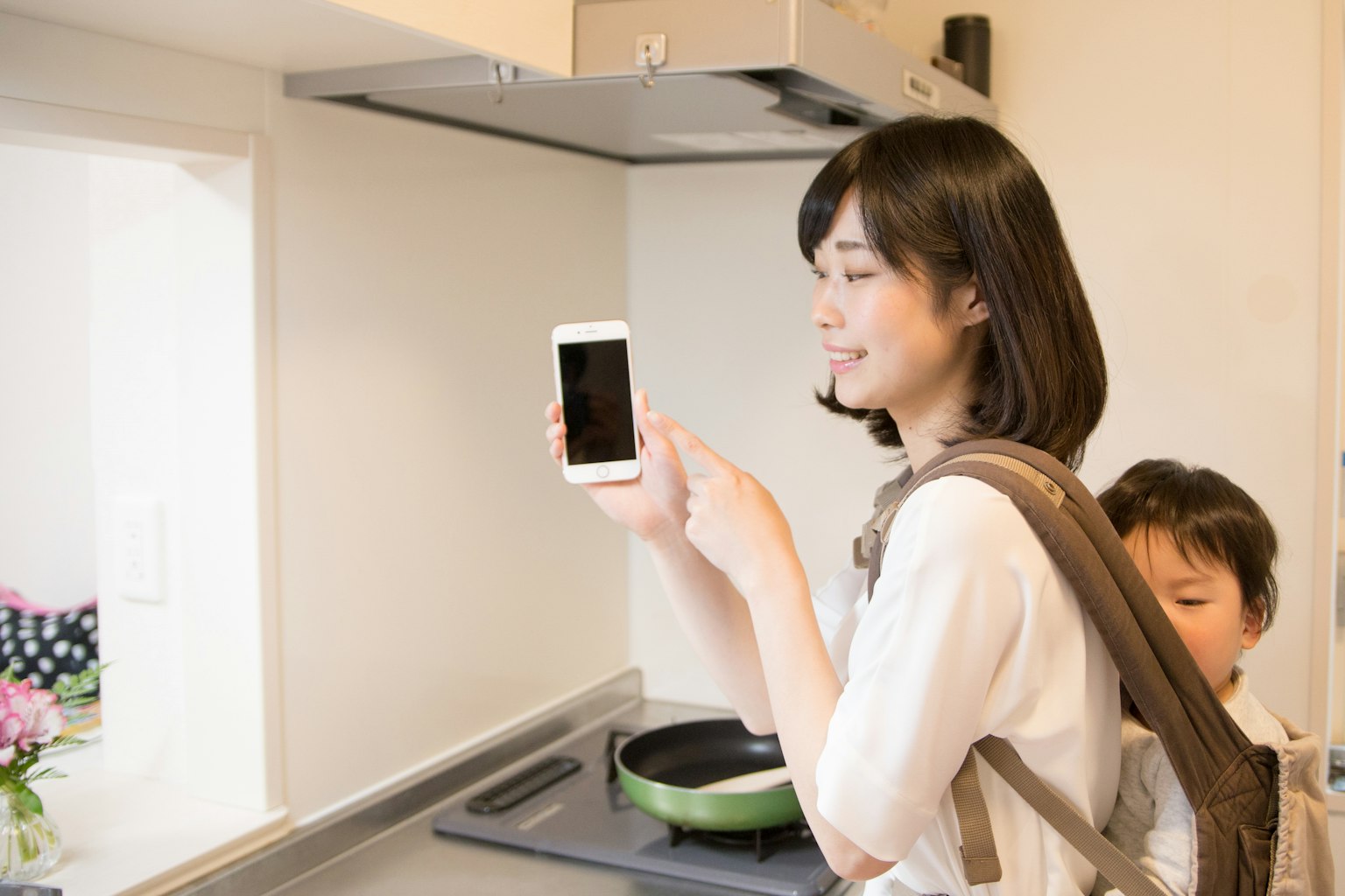 Une femme tenant un smartphone dans une cuisine avec un enfant derrière elle