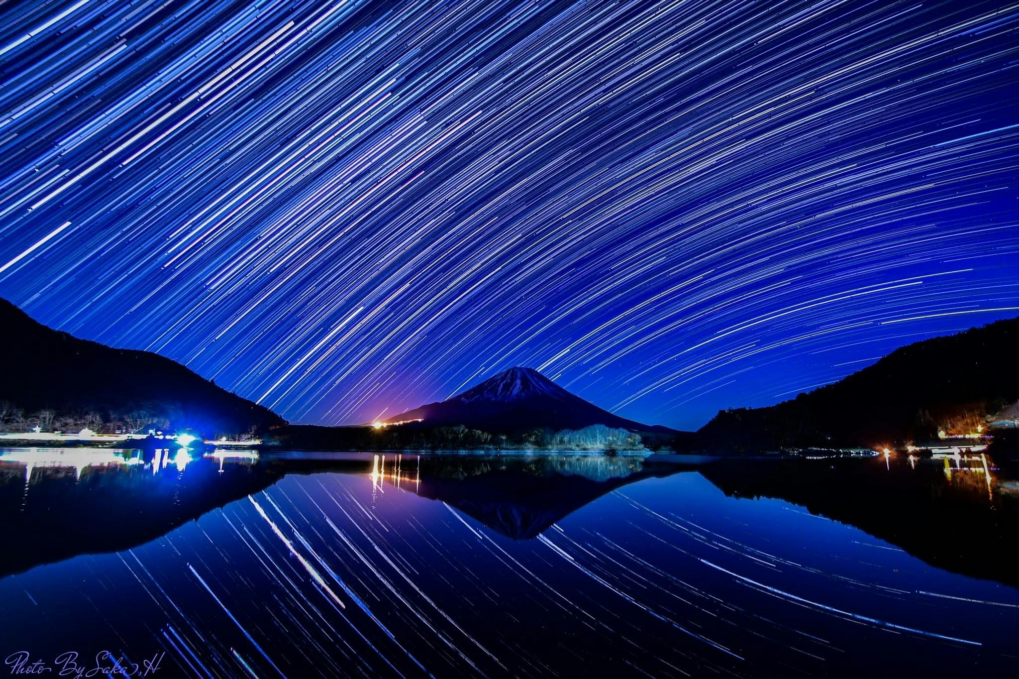 精進湖の夜空に広がる星の軌跡と富士山のシルエット