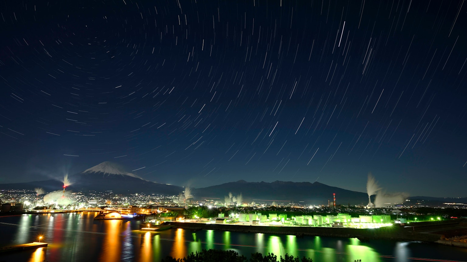 Beautiful landscape featuring flowing stars over Mount Fuji and city lights at night