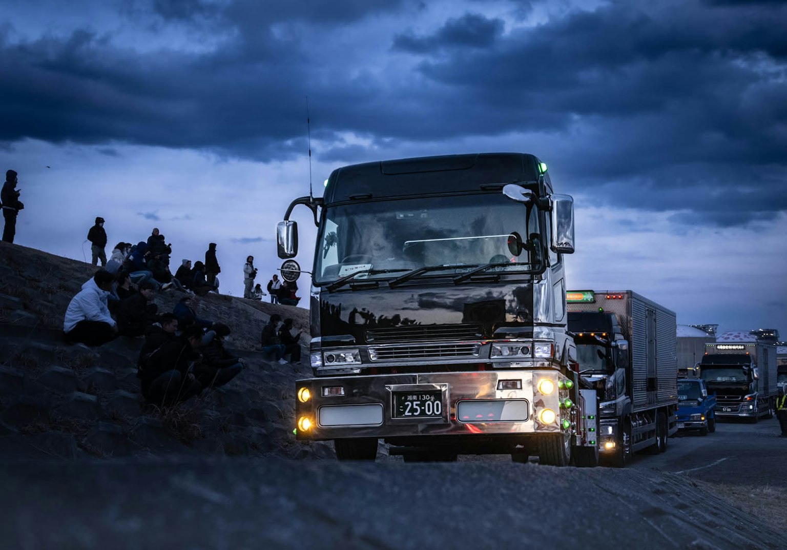 Scene of a truck parked on a highway at night with people sitting nearby