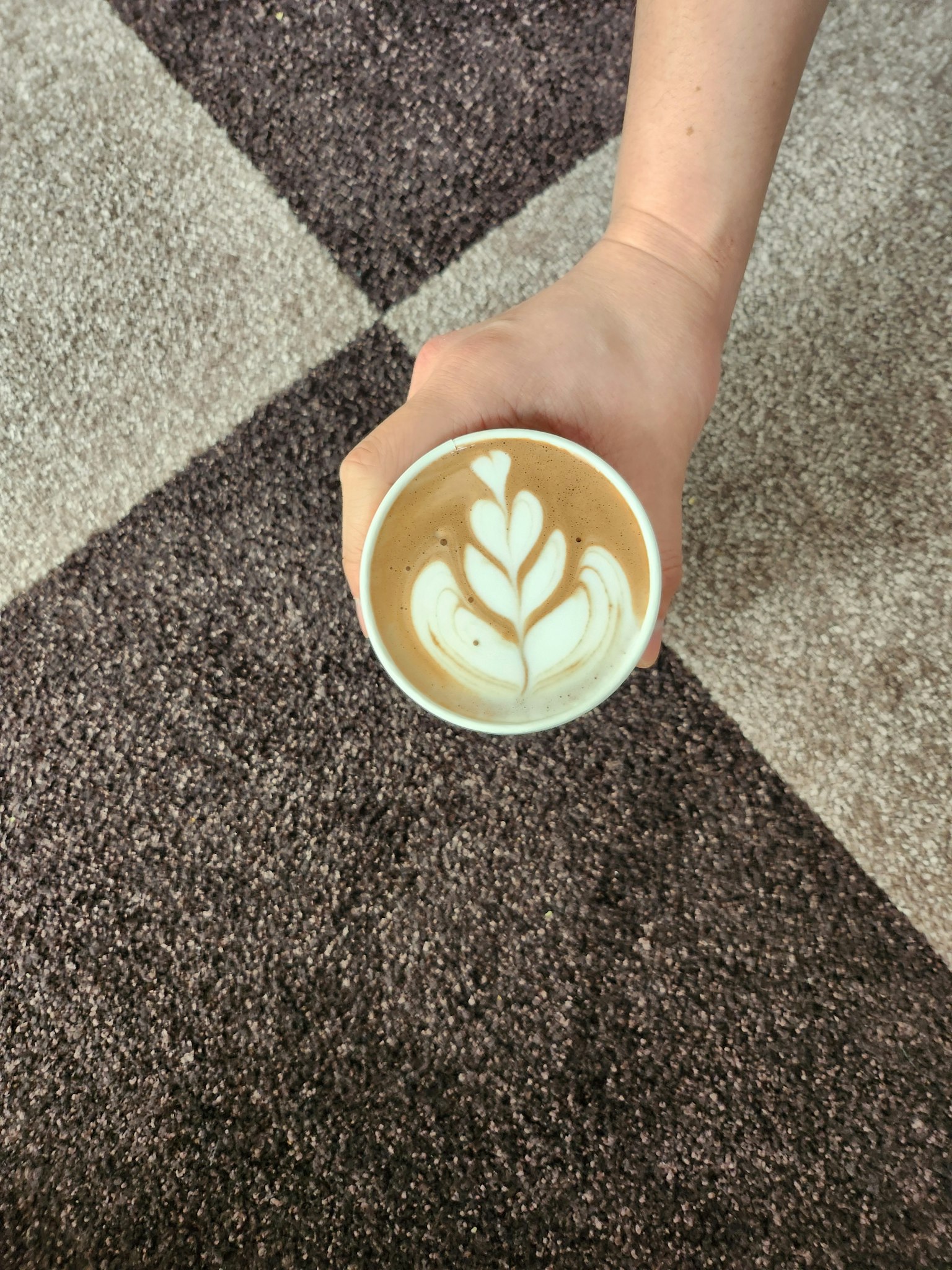 手中拿着一杯咖啡杯，上面有拉花，背景是地毯