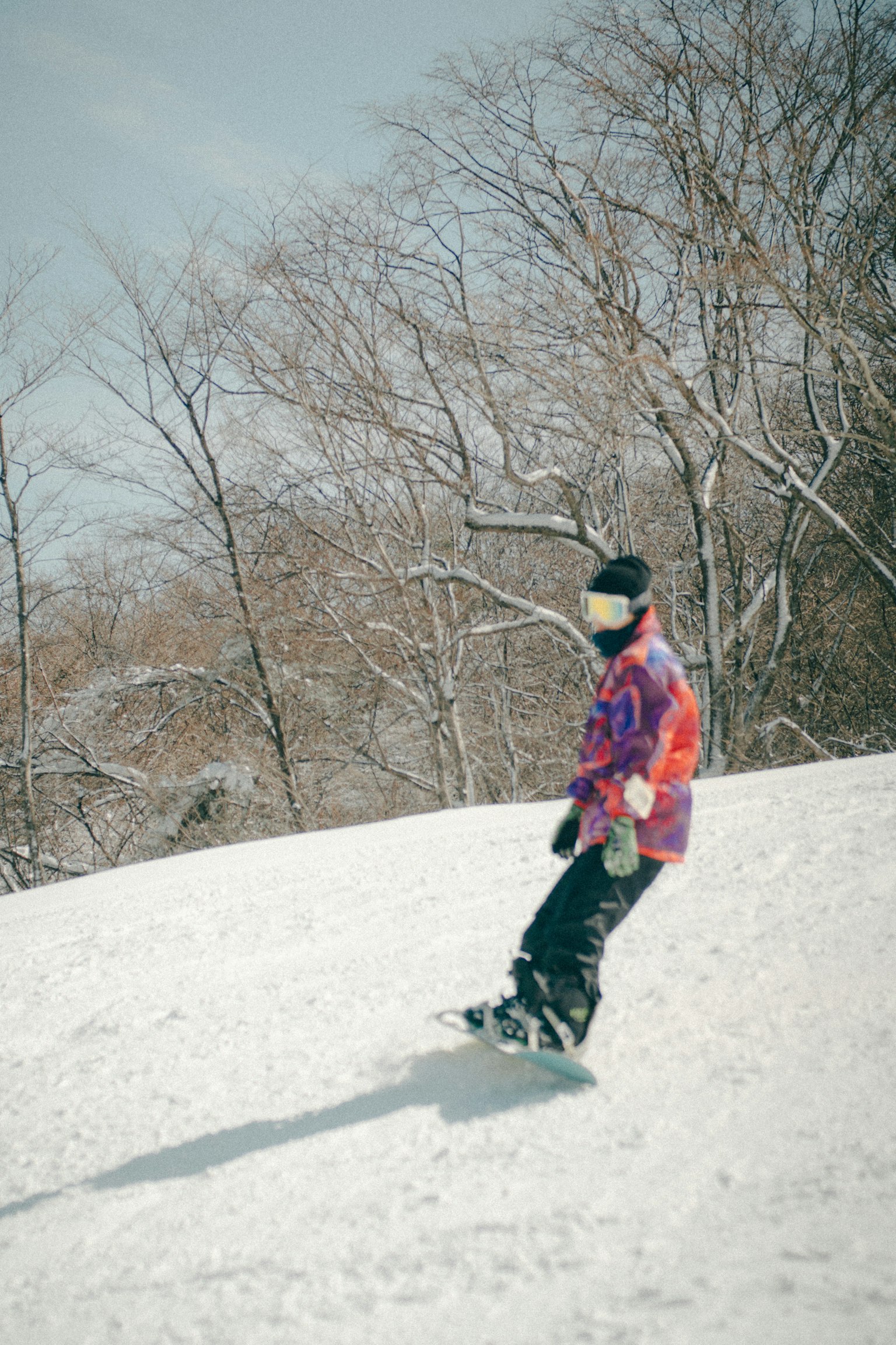 Persona practicando snowboard en una pendiente nevada con una chaqueta colorida
