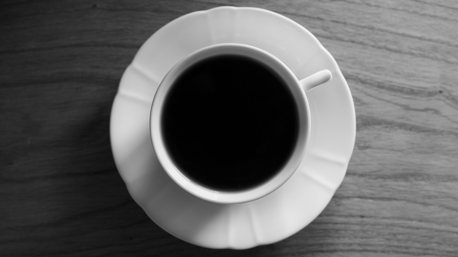 Draufsicht auf schwarzen Kaffee in einer weißen Tasse auf einem Holztisch