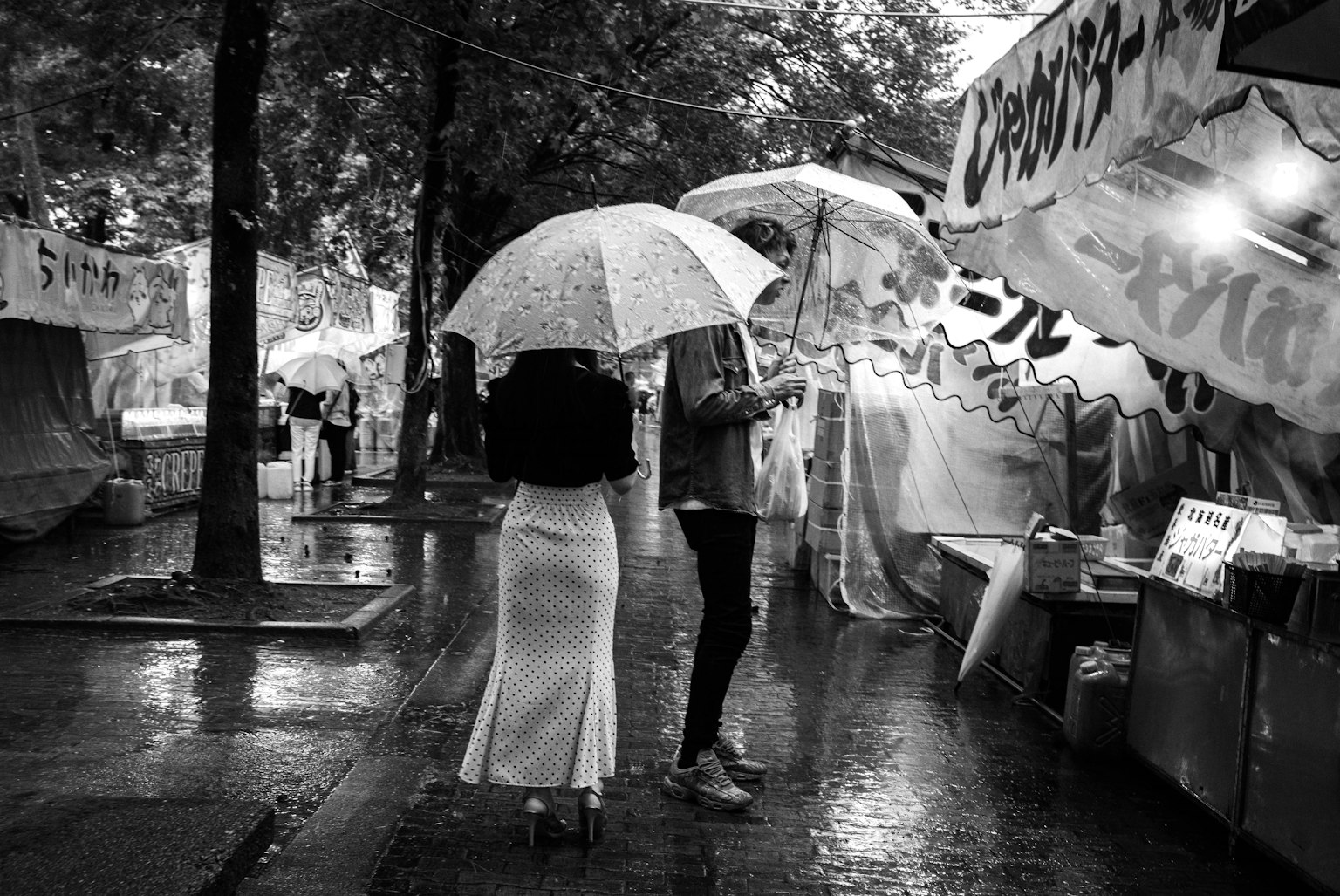 Black and white street scene with two people holding umbrellas in the rain