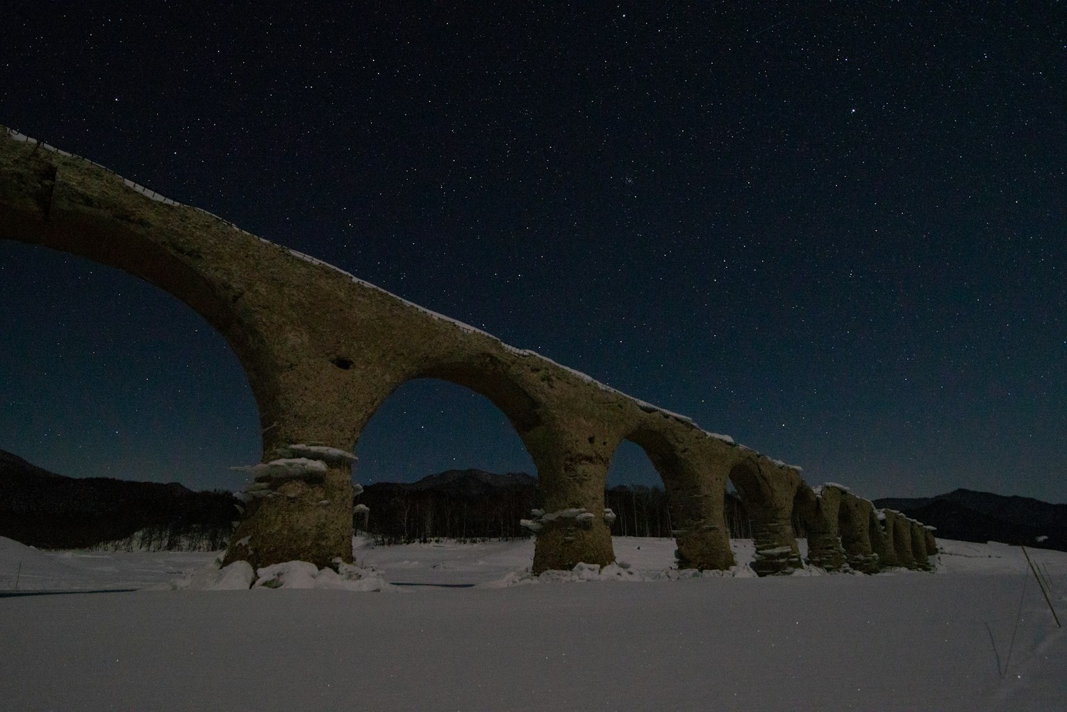 Acueducto antiguo cubierto de nieve bajo un cielo estrellado