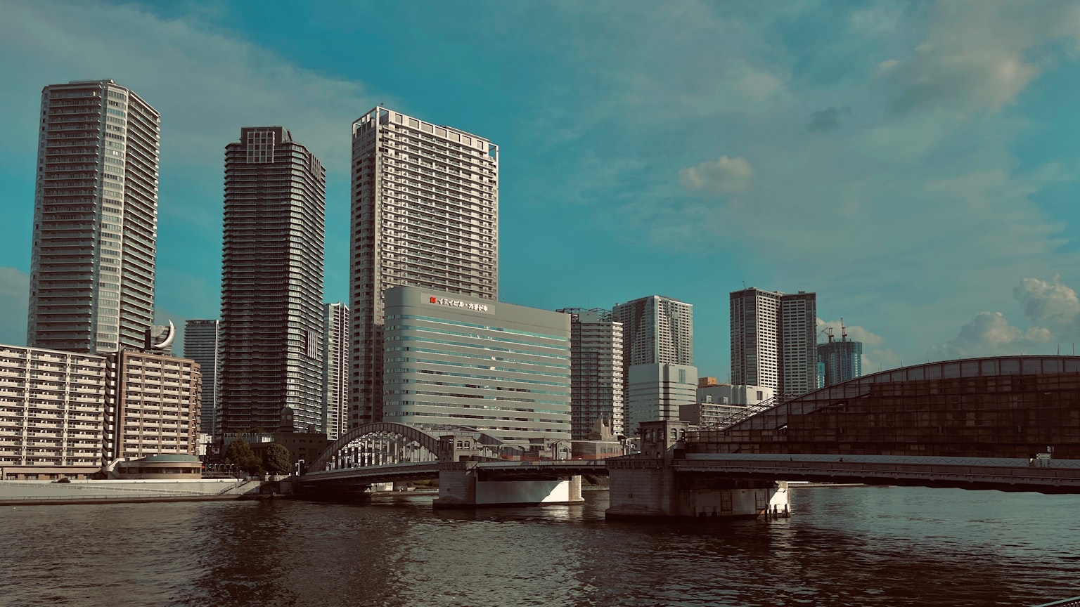 เส้นขอบฟ้าของเมืองที่มีตึกสูงและแม่น้ำใต้ท้องฟ้าสีฟ้า