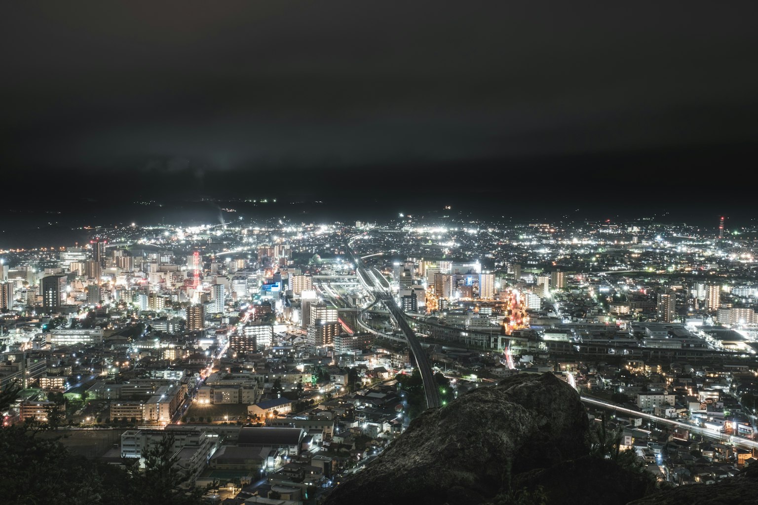 Panoramablick auf eine Stadt bei Nacht mit hellen Gebäudelichtern und einem entfernten Riesenrad
