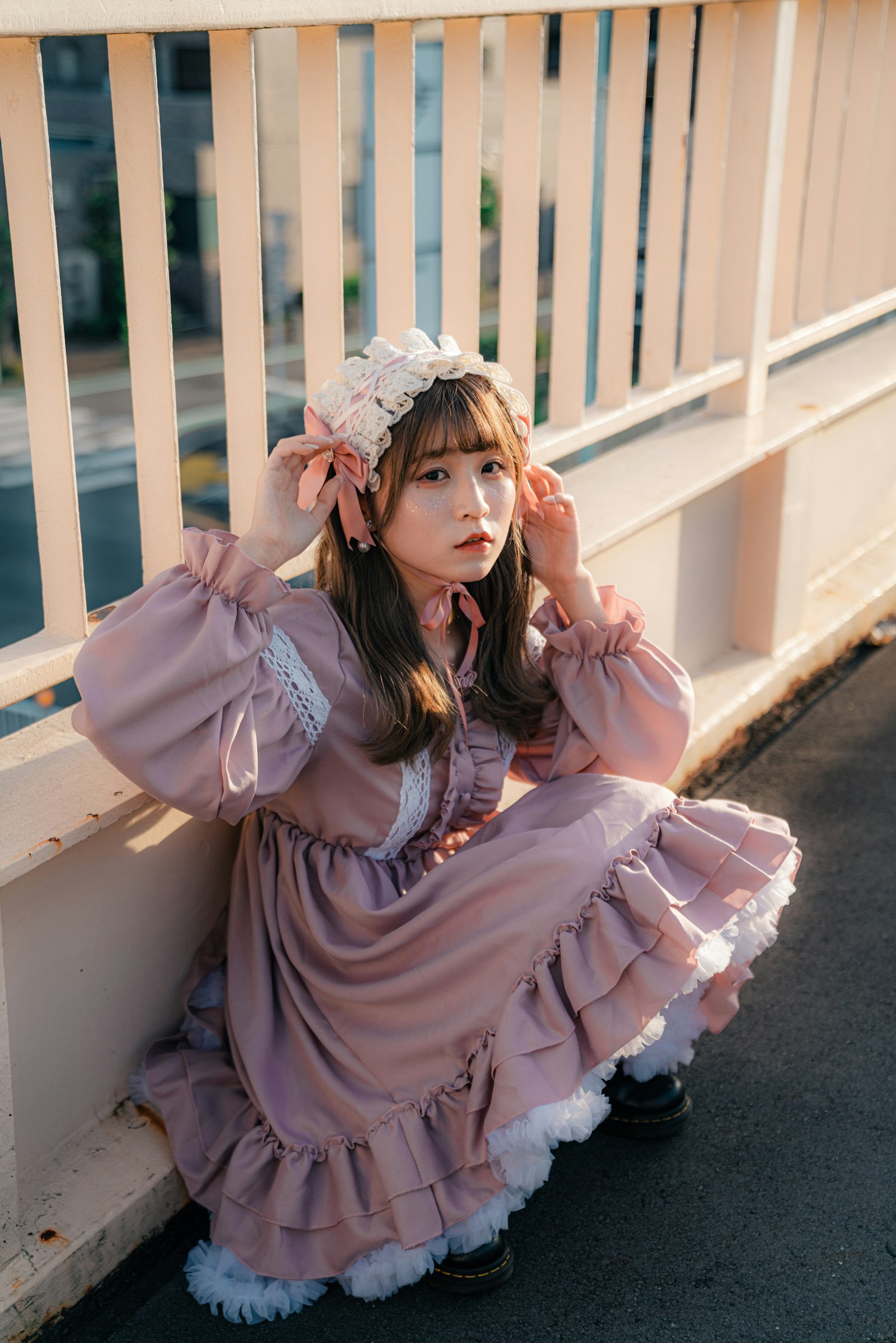 Una niña con un vestido rosa y un accesorio floral en el cabello sentada contra una barandilla