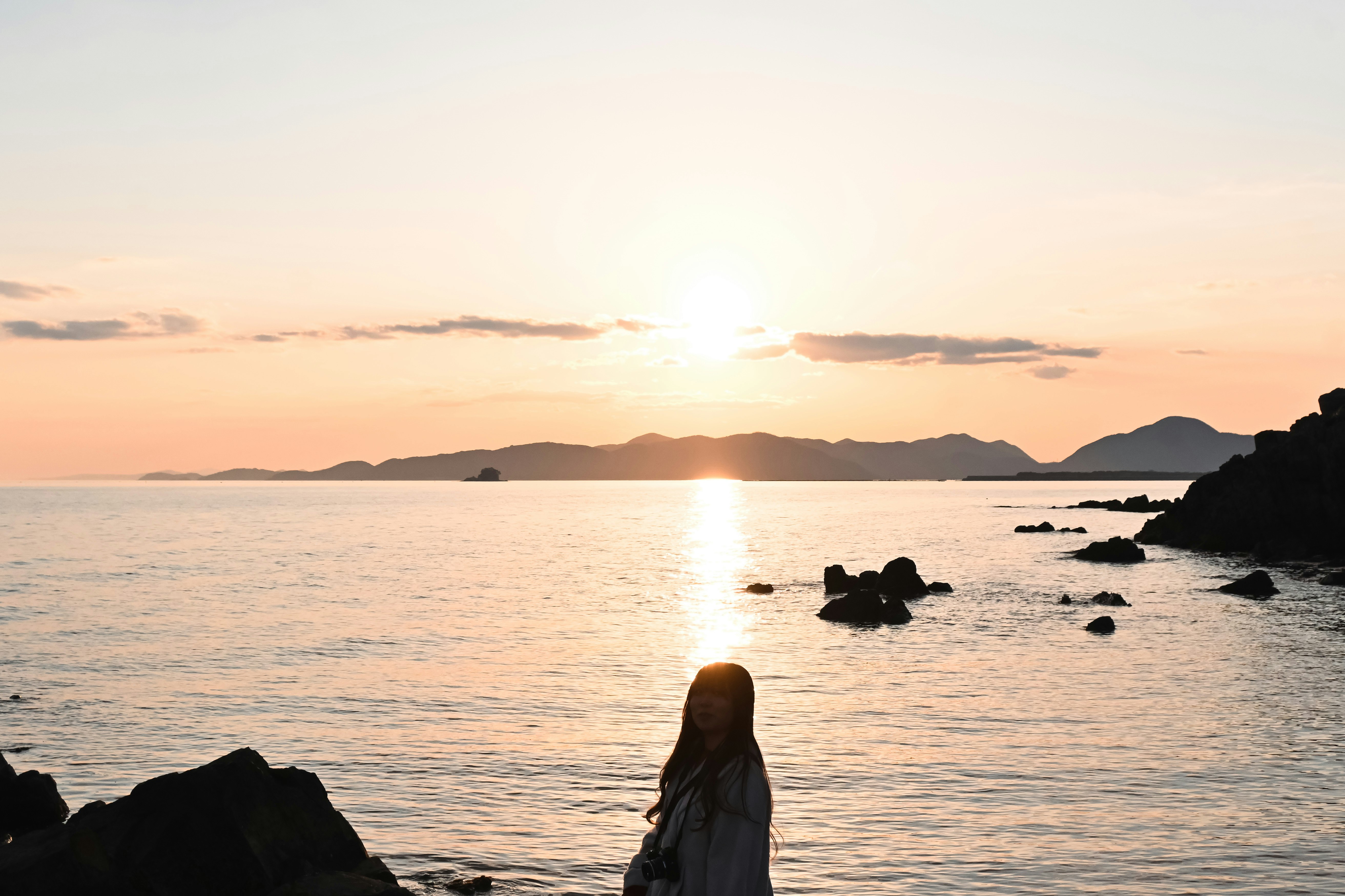 夕日に照らされる海辺の岩場と水平線