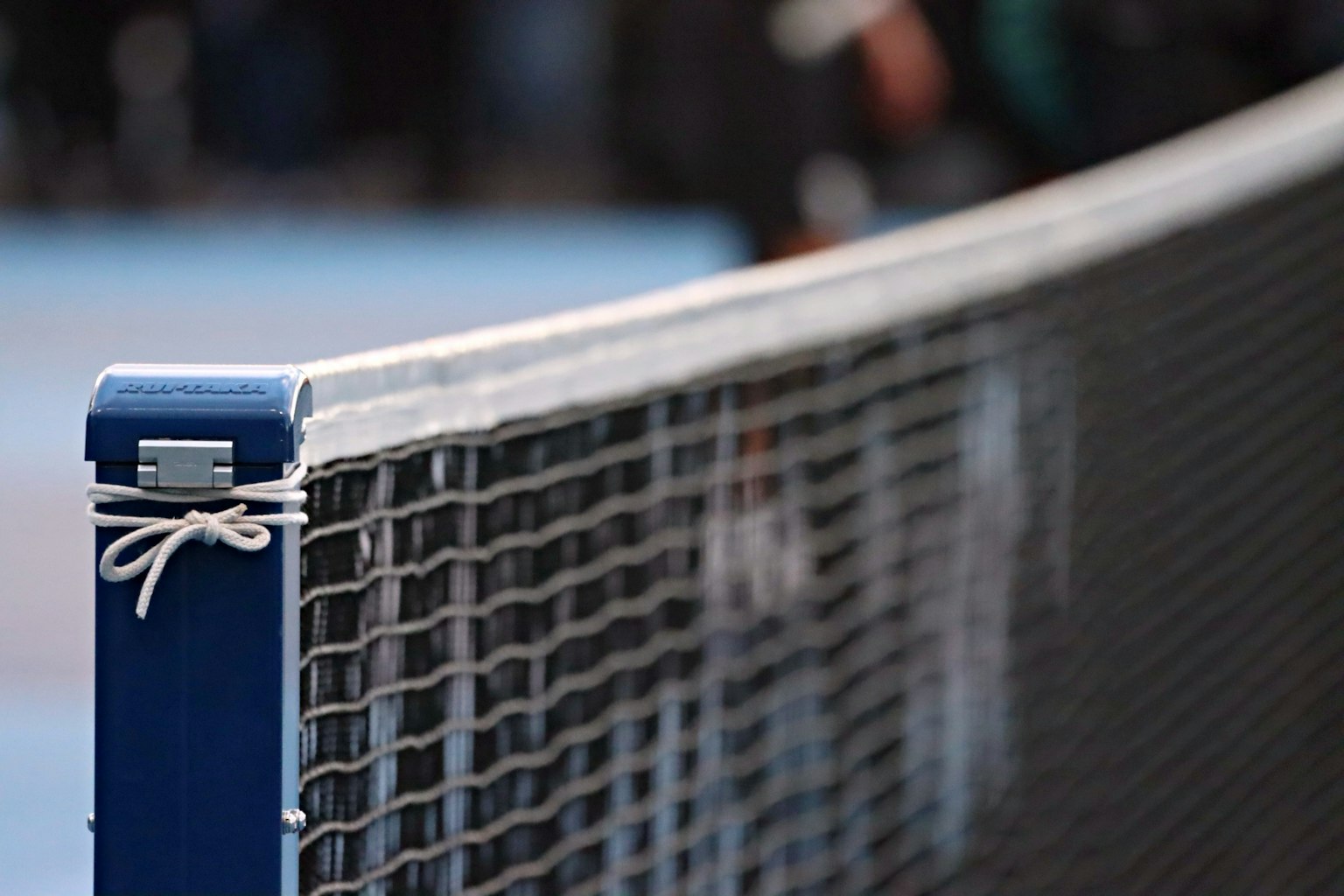 Foto close-up jaring tenis menunjukkan tiang biru dan jaring putih