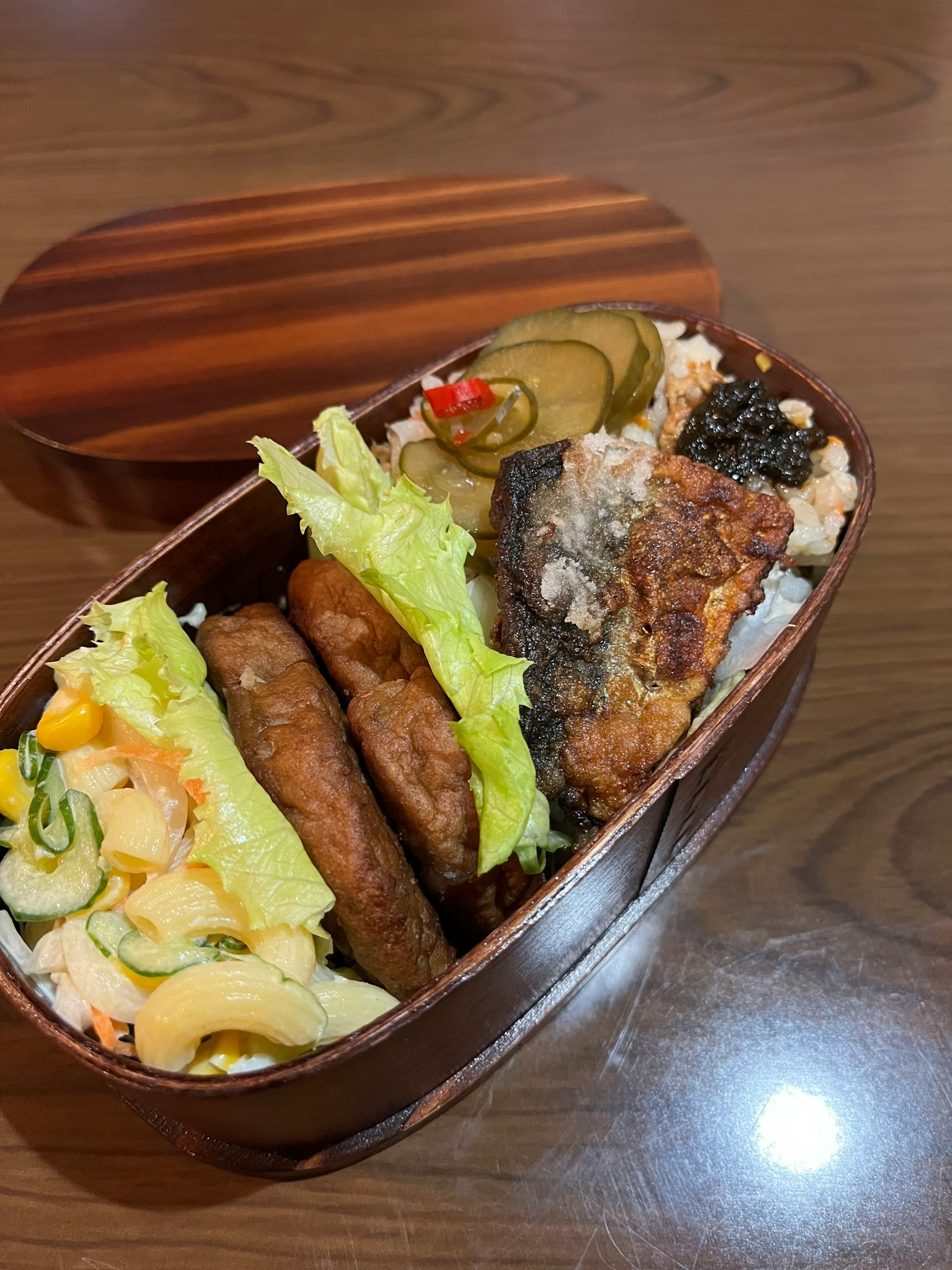 Boîte à bento en bois remplie de poisson grillé, galettes de viande et salade de légumes