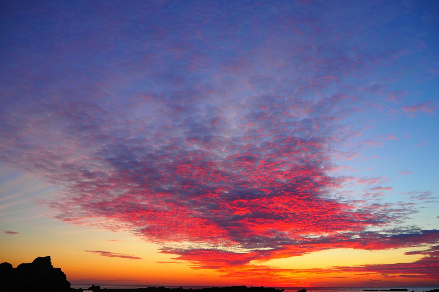 Langit matahari terbenam yang menakjubkan dengan awan merah cerah dan pemandangan pantai