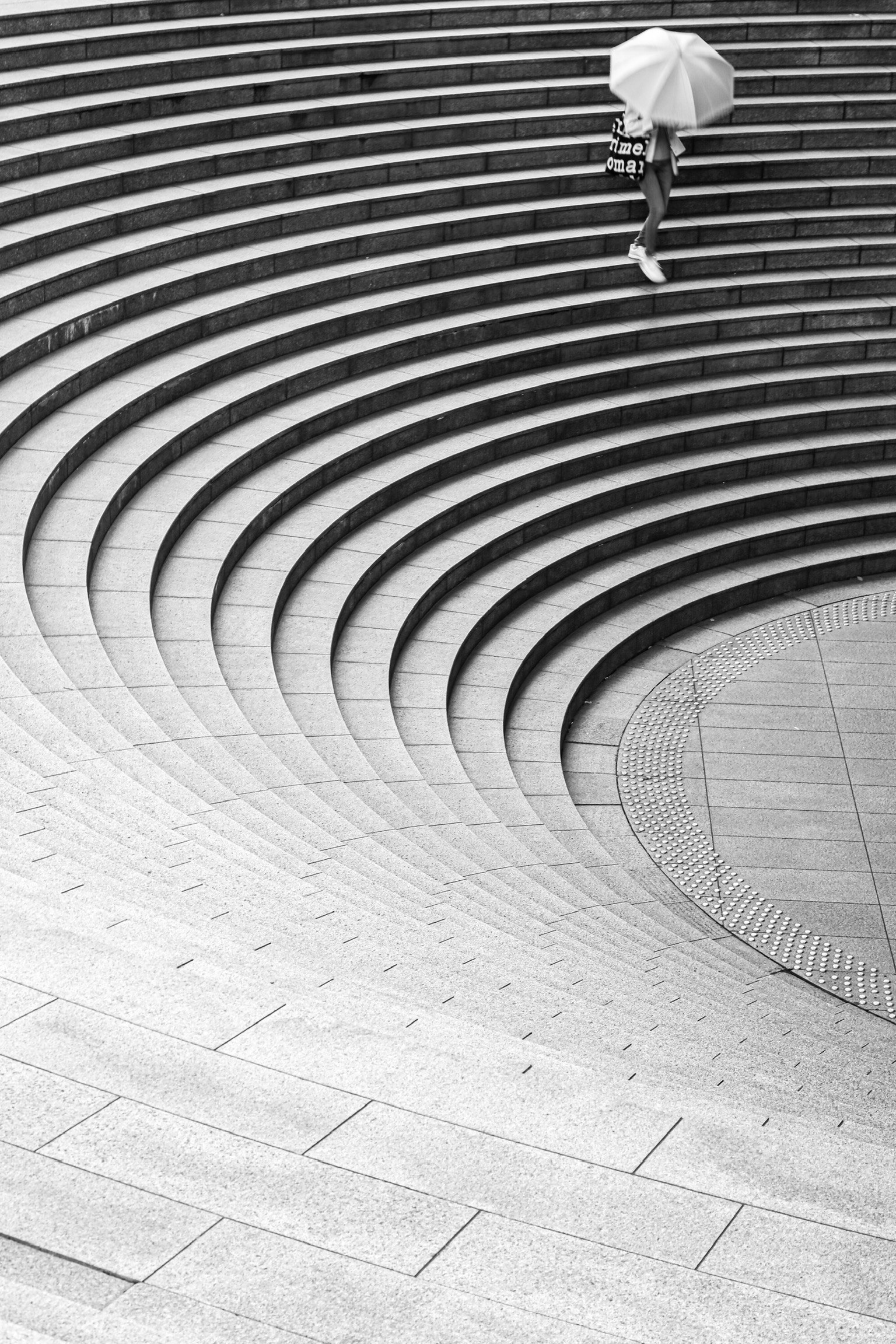 一幅黑白图像，显示一个人拿着伞走上圆形楼梯