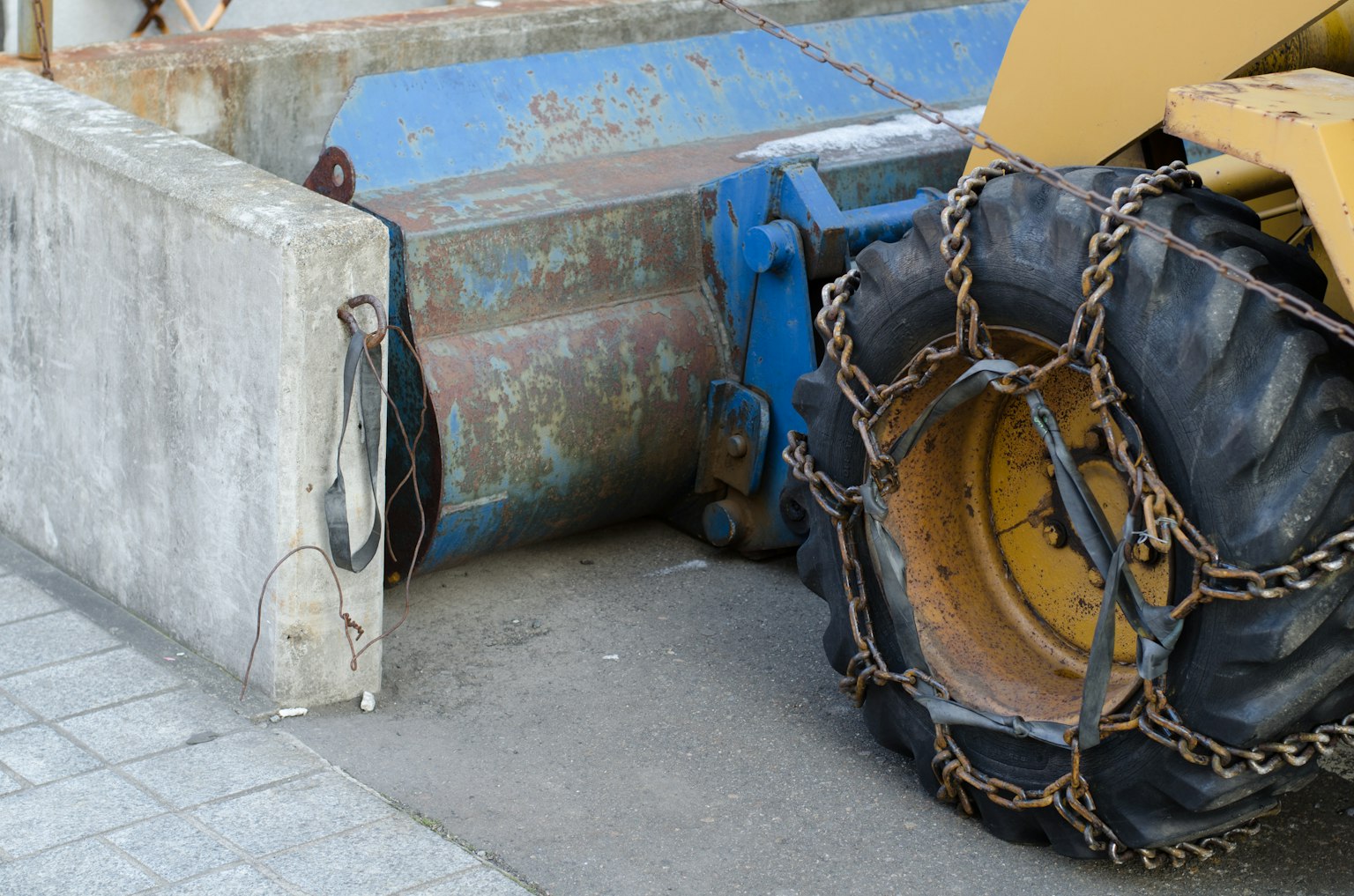 Yellow construction vehicle tire with chain attached next to concrete block at construction site