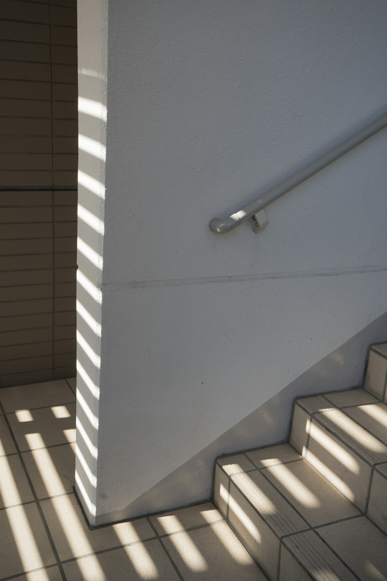 Pared blanca con pasamanos de escalera y patrones de luz y sombra llamativos