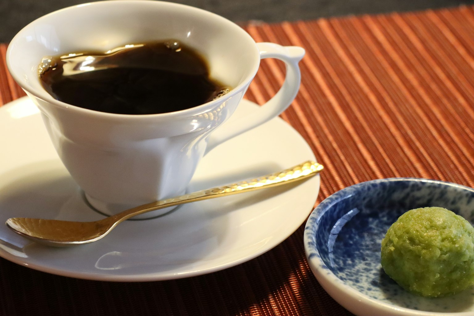 Café noir dans une tasse blanche avec un bonbon vert sur une assiette bleue