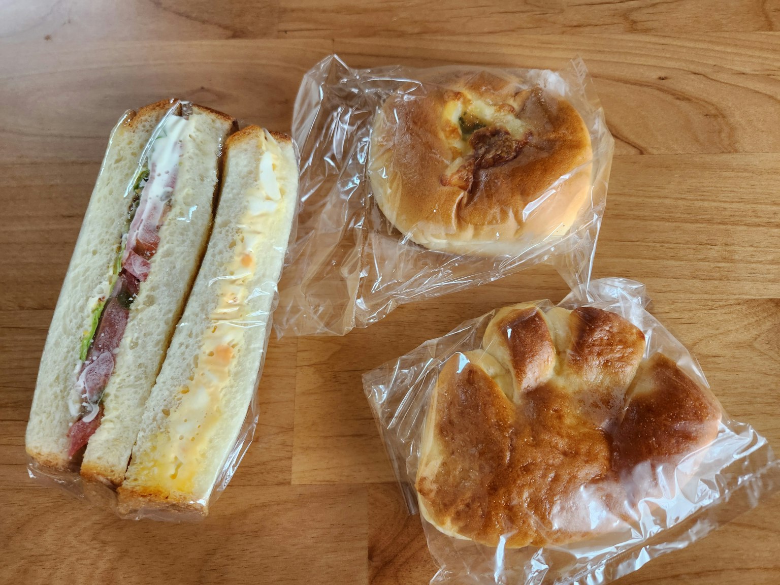 一个三明治和两个烘焙食品用塑料包装放在木桌上