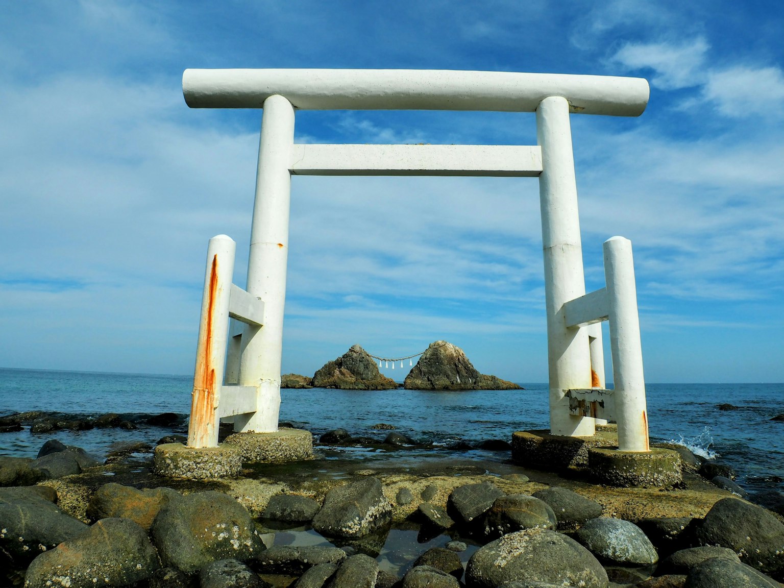 Gerbang torii putih dengan pantai berbatu dan langit biru