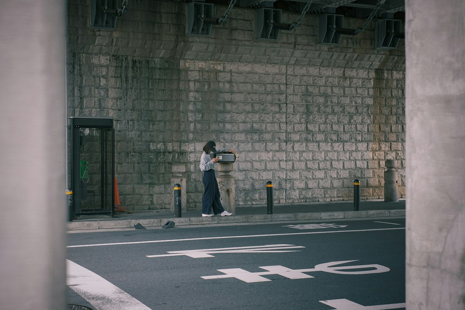 Persona in piedi sotto un muro di cemento con testo bianco sulla strada vicina
