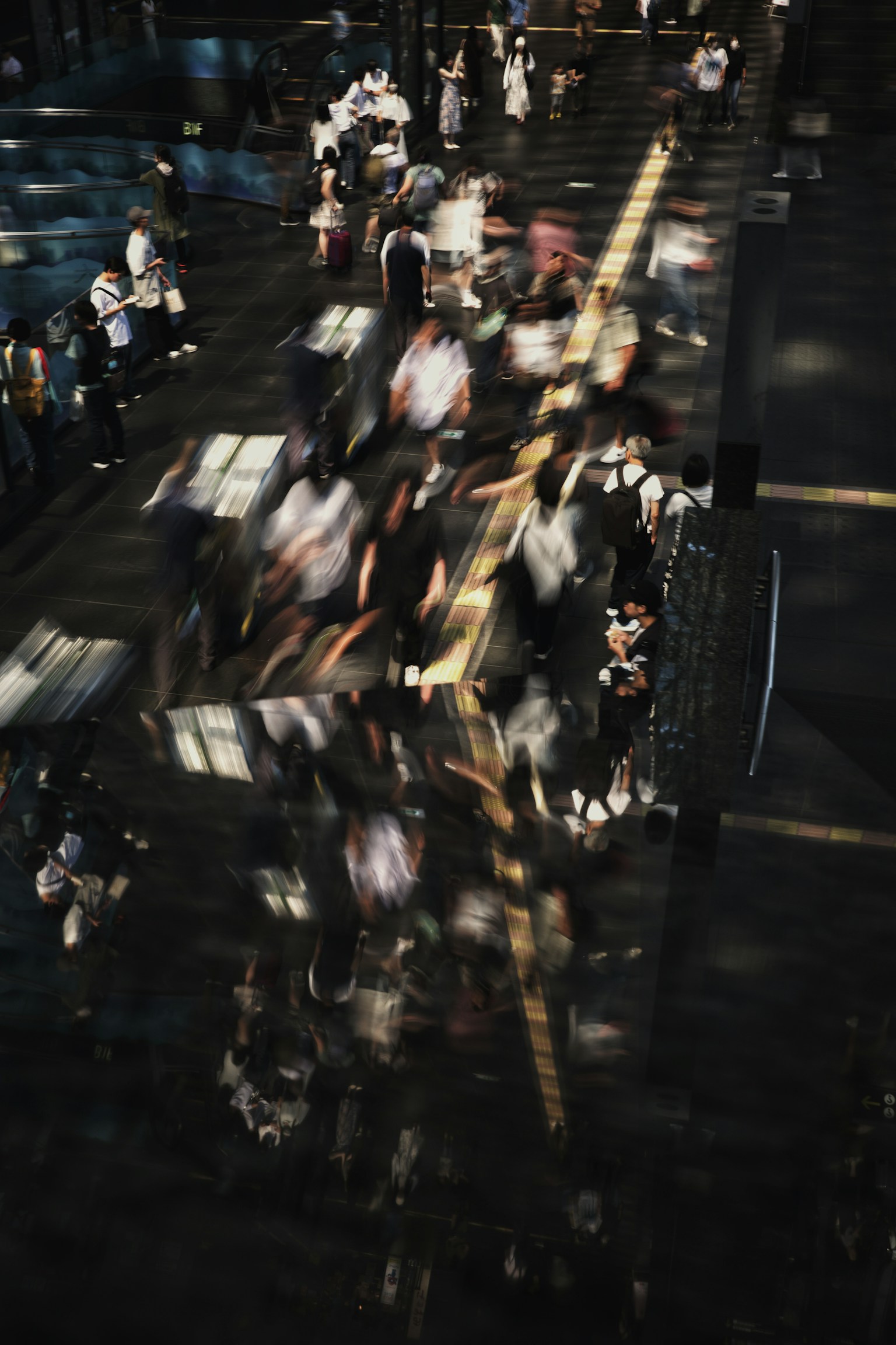 Immagine sfocata di persone in movimento in una stazione con riflessi di luce e ombre sorprendenti