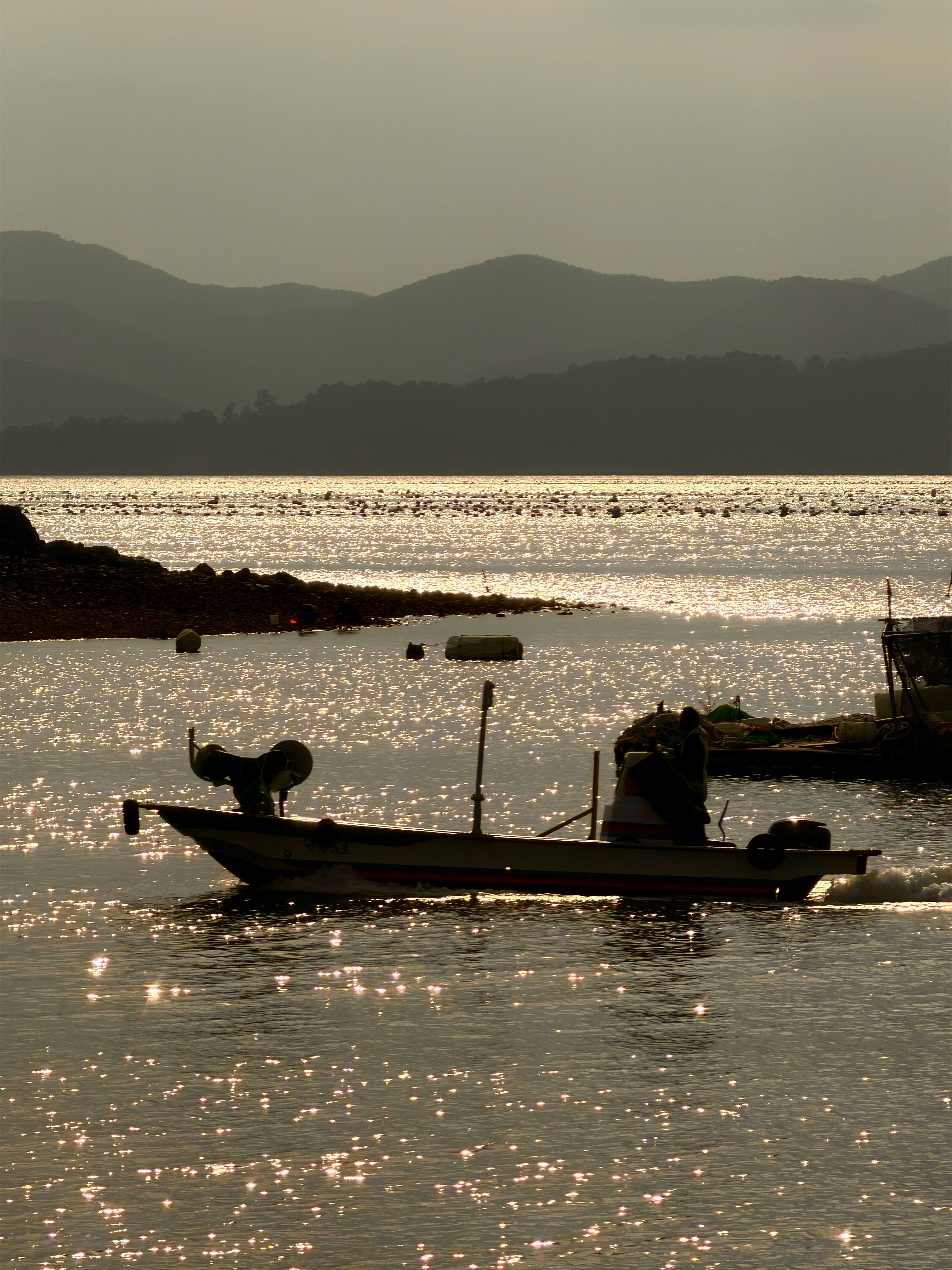 夕暮れの海辺に浮かぶ小舟と遠くの山並み