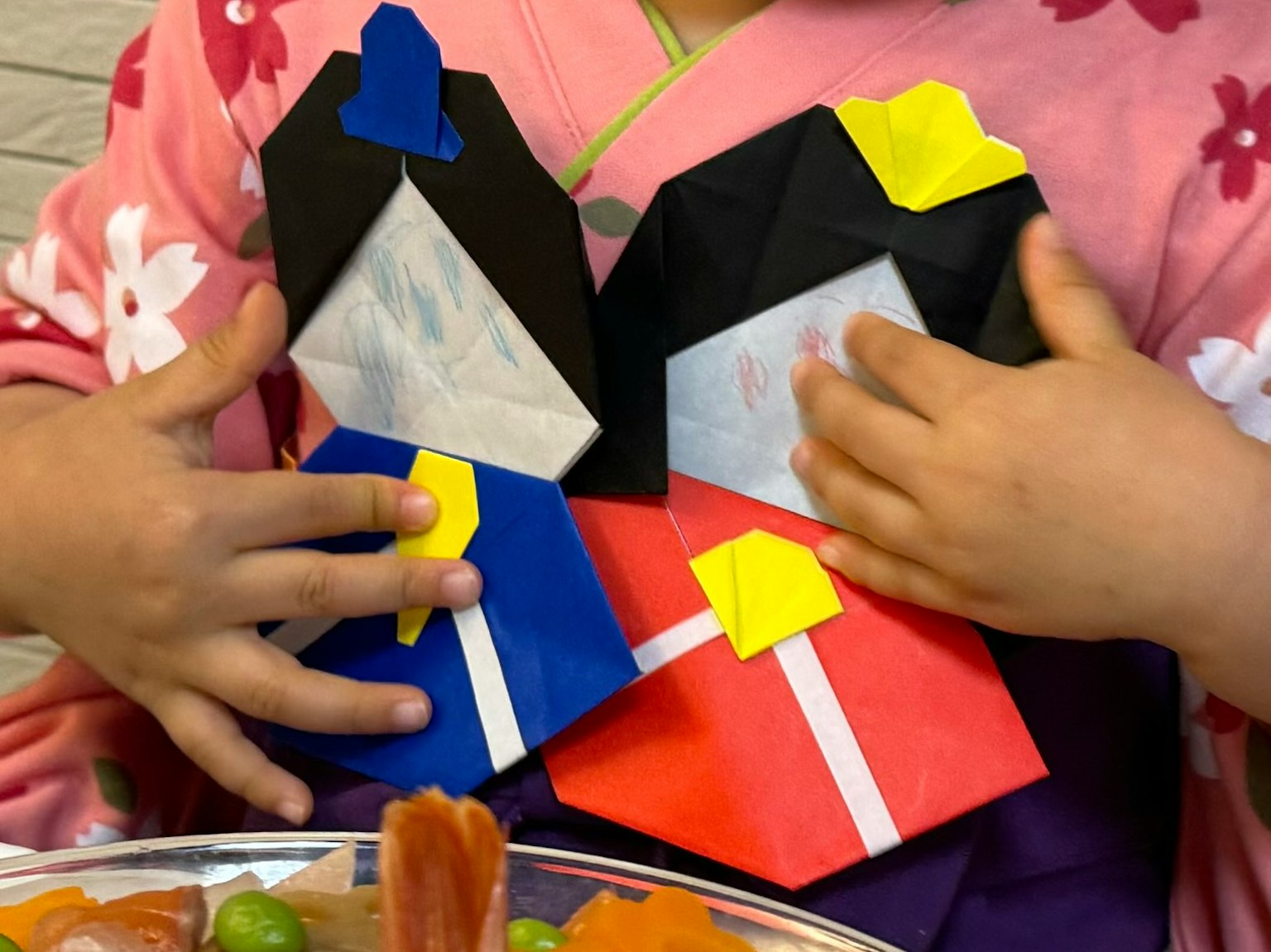 Kind hält zwei Origami-Puppen in bunten Outfits
