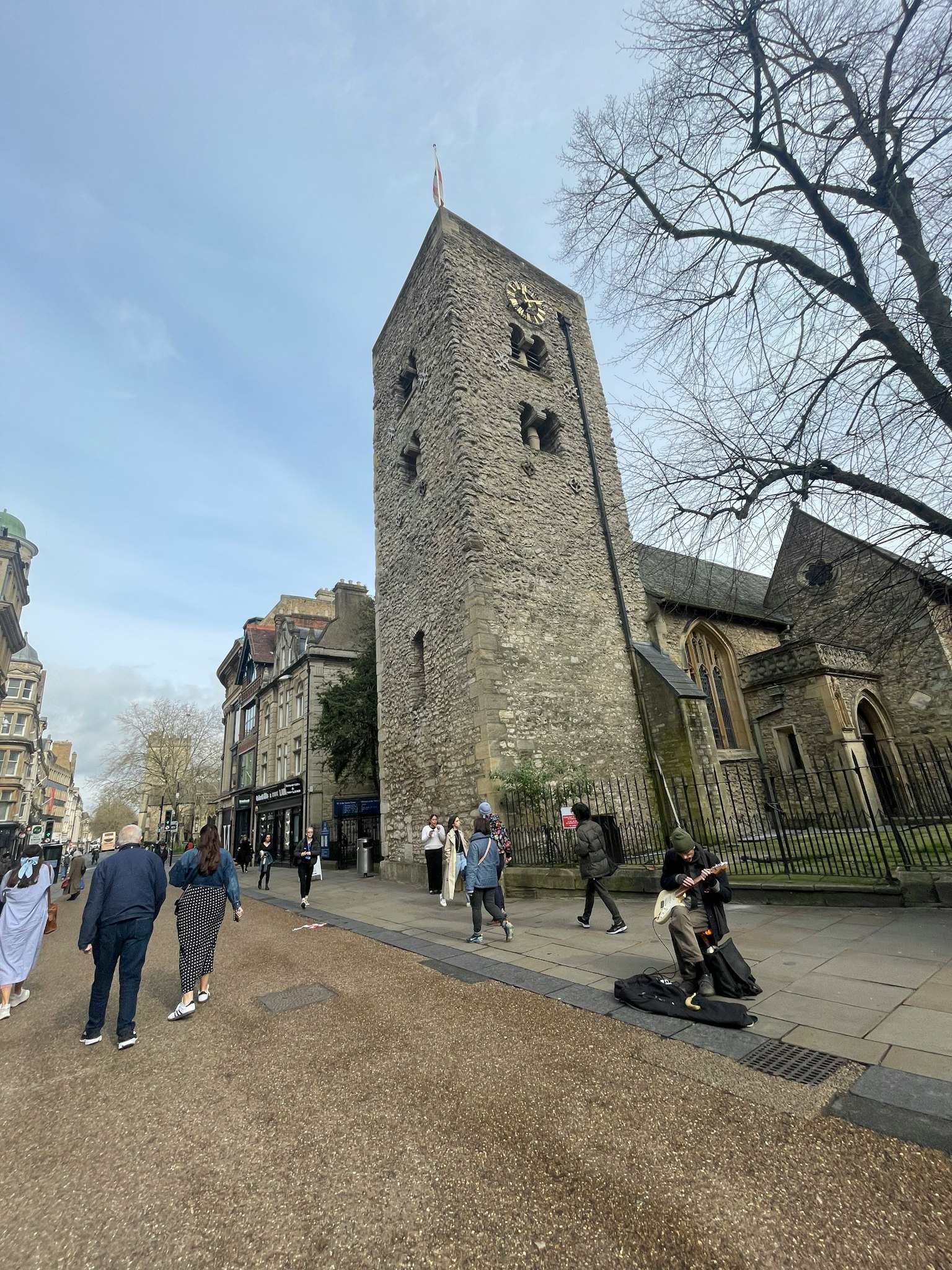 Steinturm und historische Gebäude entlang einer Straße mit gehenden Menschen