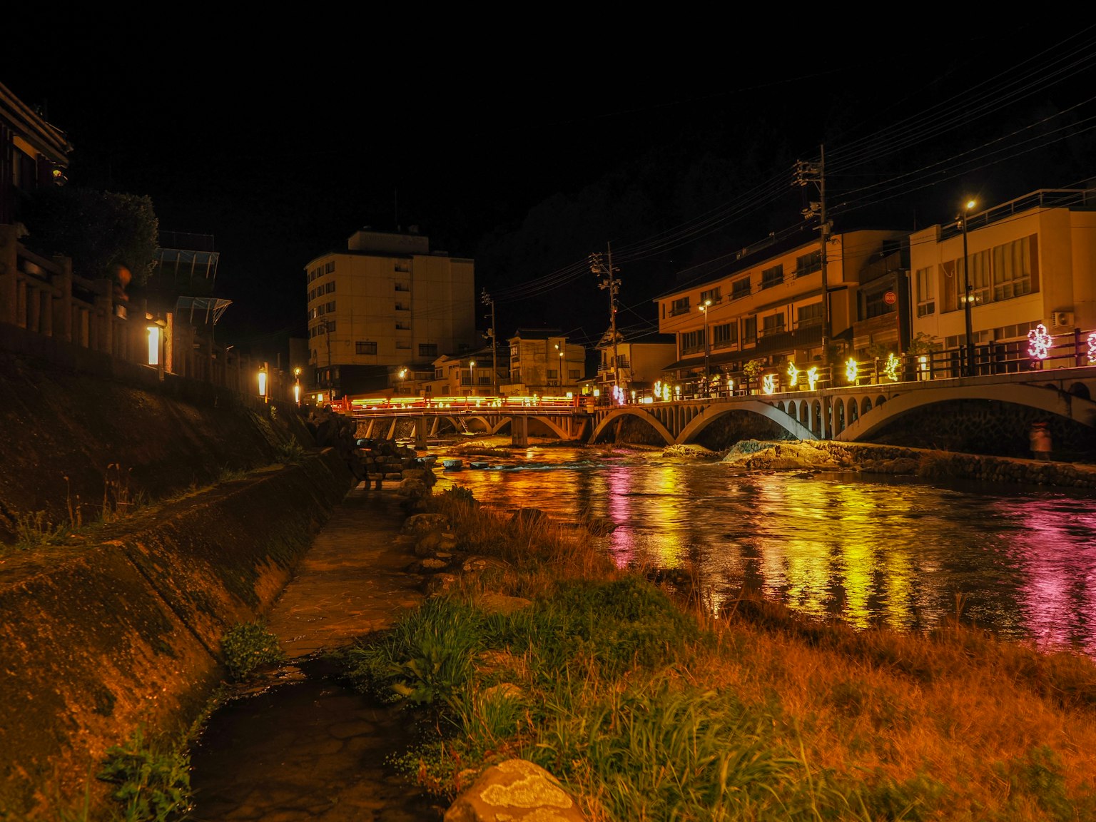 Nighttime riverside scene with illuminated bridge and buildings