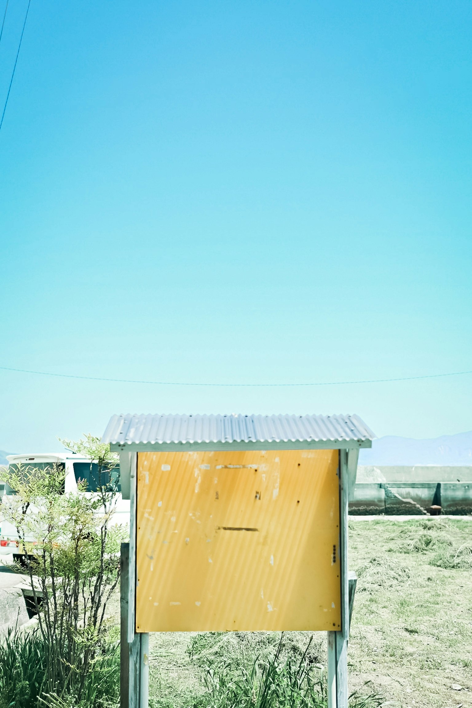 An old yellow mailbox under a clear blue sky with surrounding grass