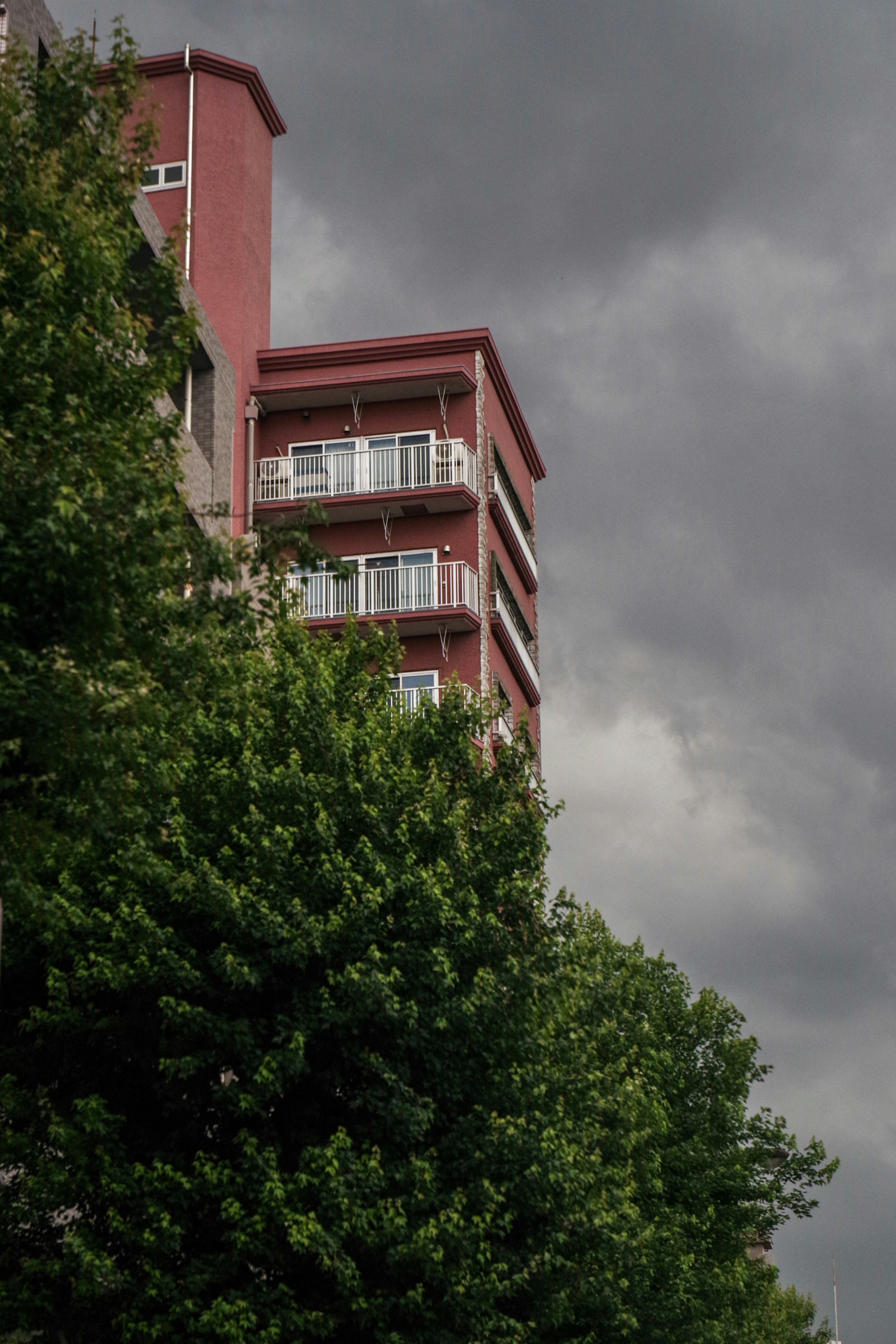 Façade d’un immeuble d’habitation rouge entourée d’arbres sous des nuages d’orage