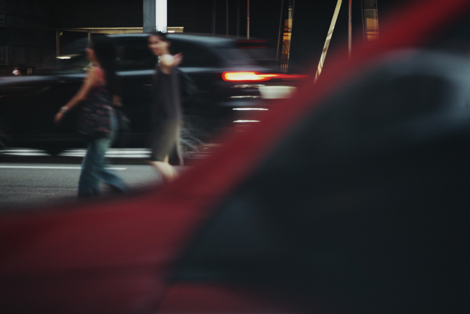 赤い車の前を歩く二人の女性のシルエットと流れる車の背景